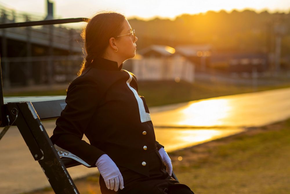 Band member in uniform rests on bleachers during golden hour.