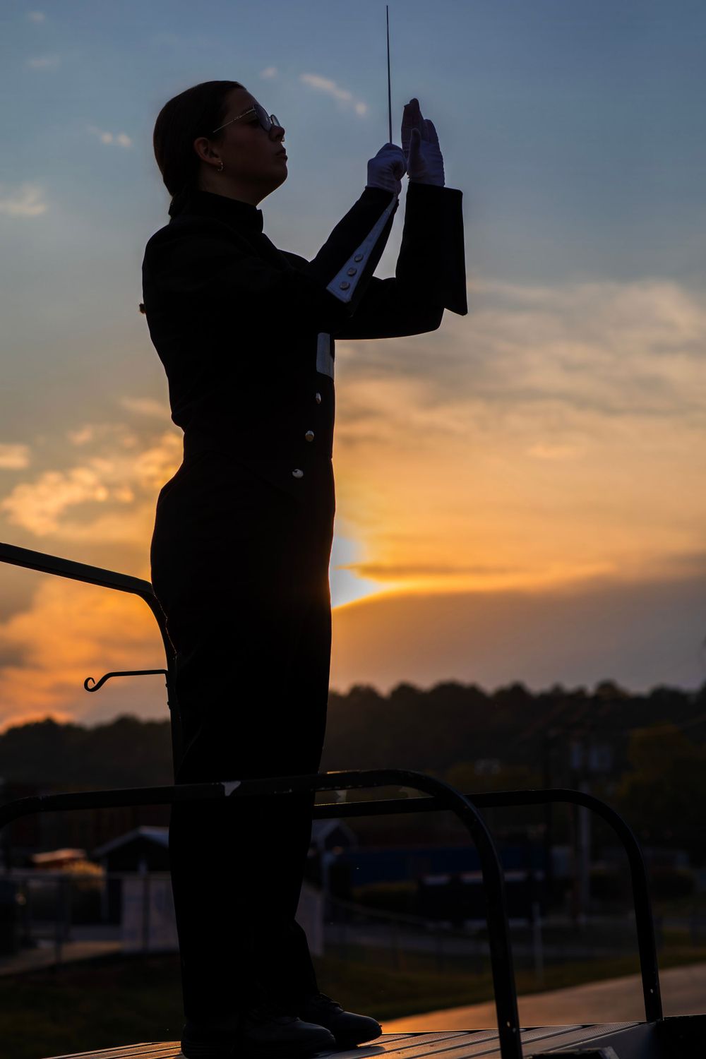 Silhouette of band conductor against vibrant sunset sky during performance.
