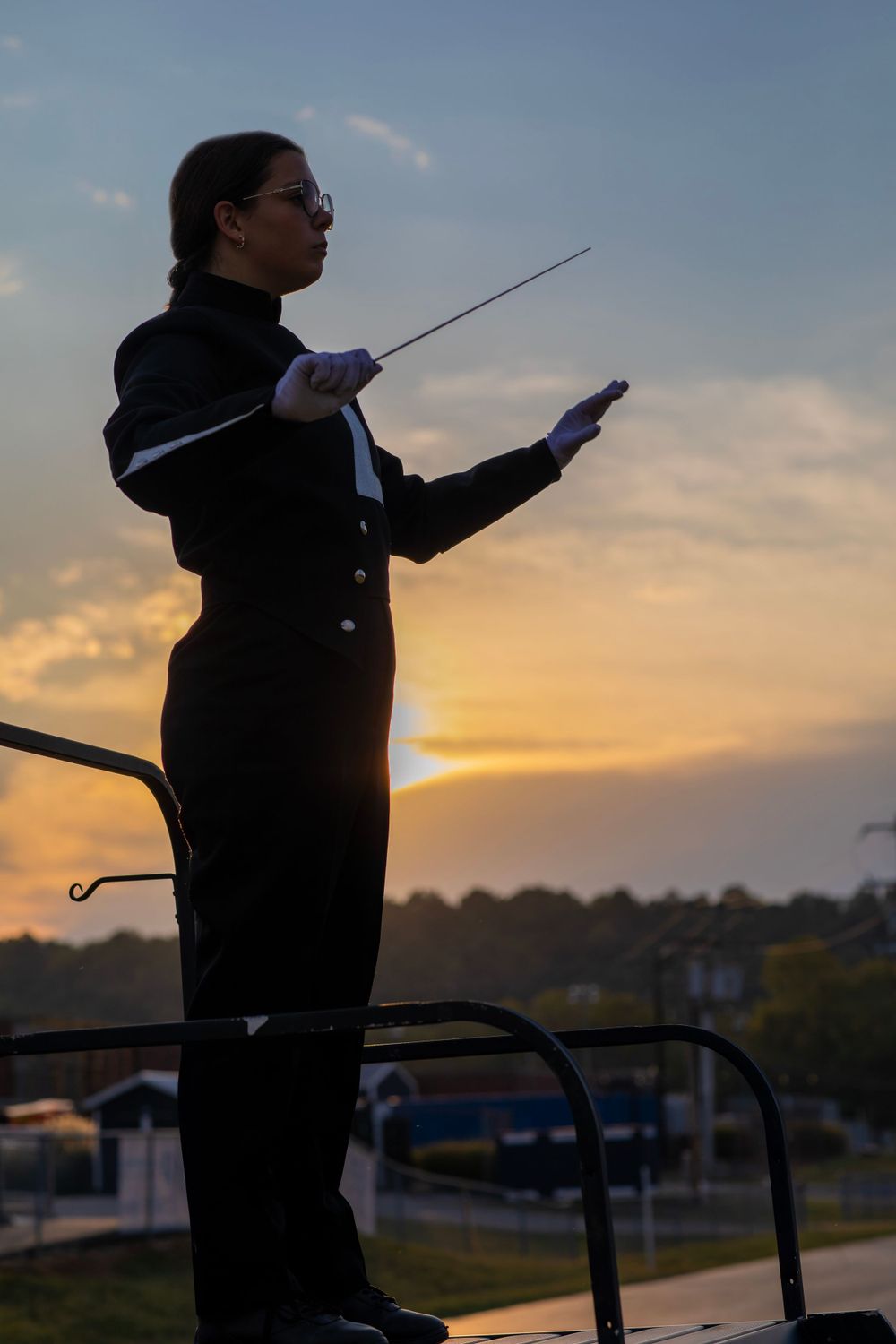 Drum major conducting at sunset with dramatic sky backdrop.