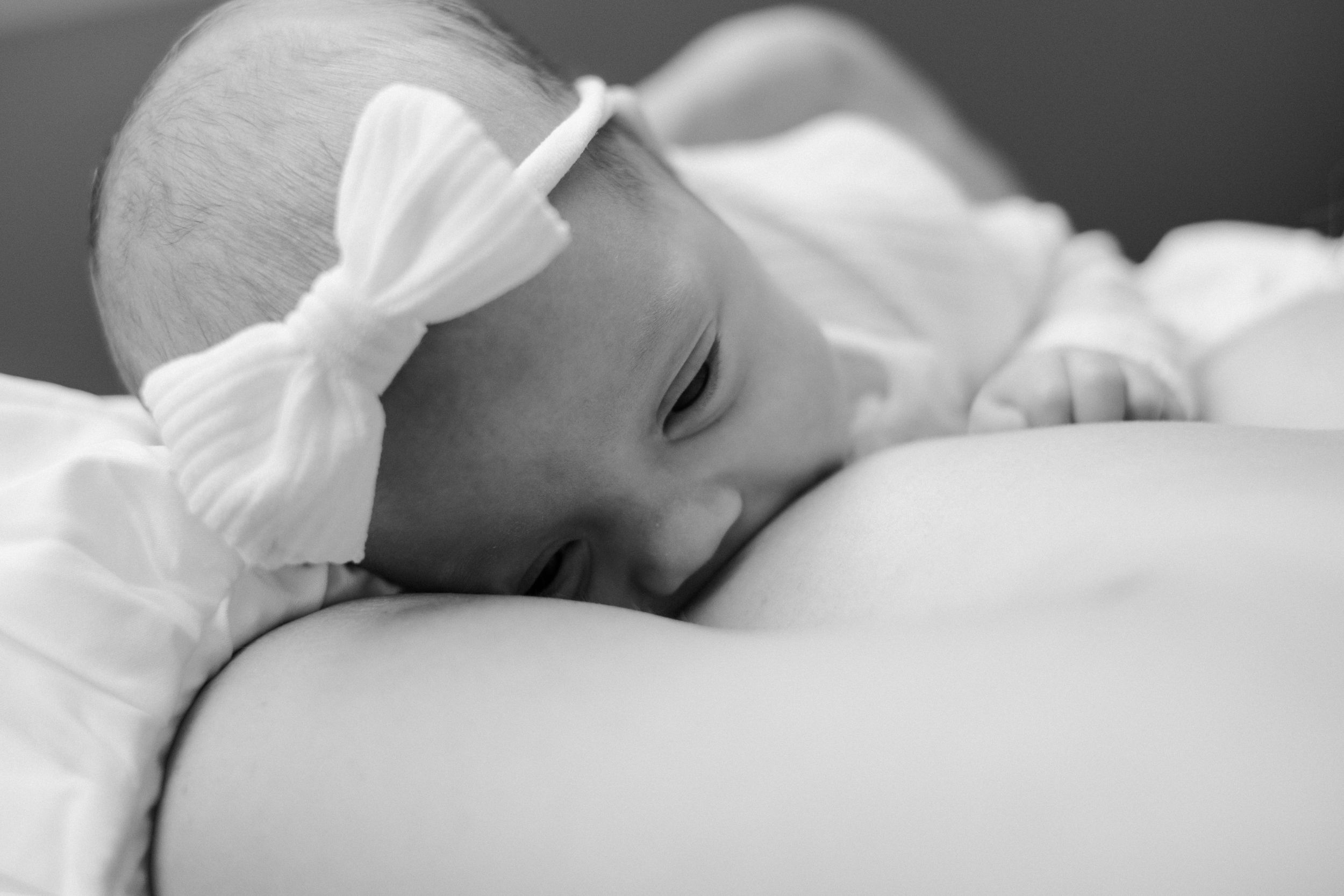Sleeping infant wearing white bow headband in black and white portrait.