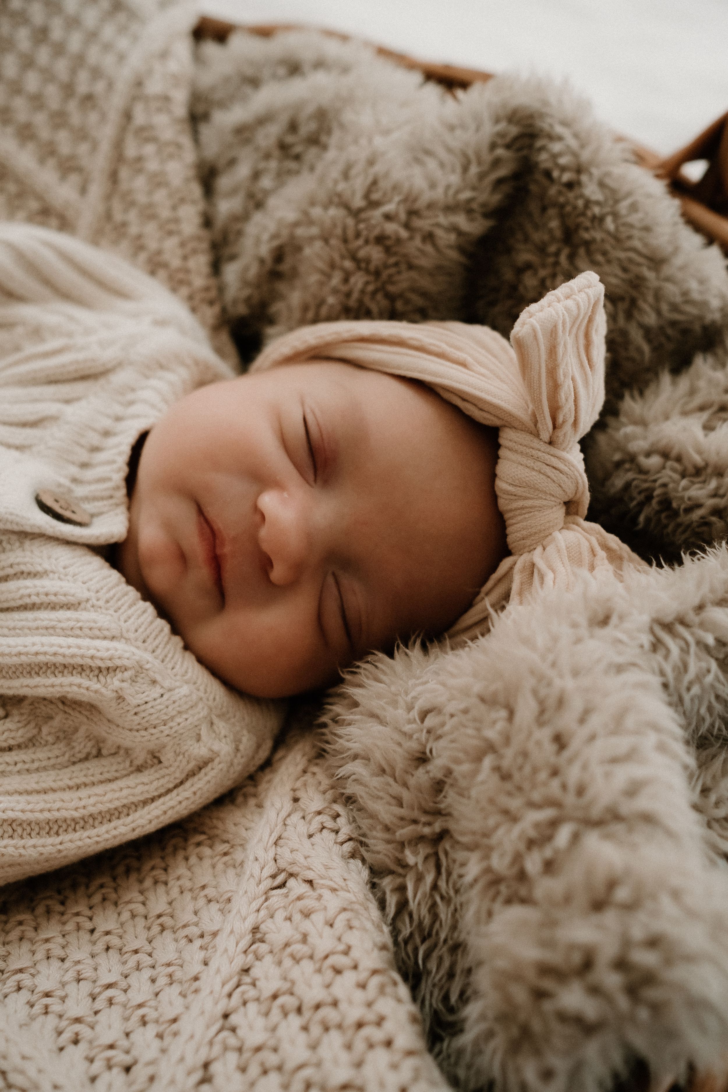 Peaceful sleeping baby with bow headband nestled in cozy knit blankets.
