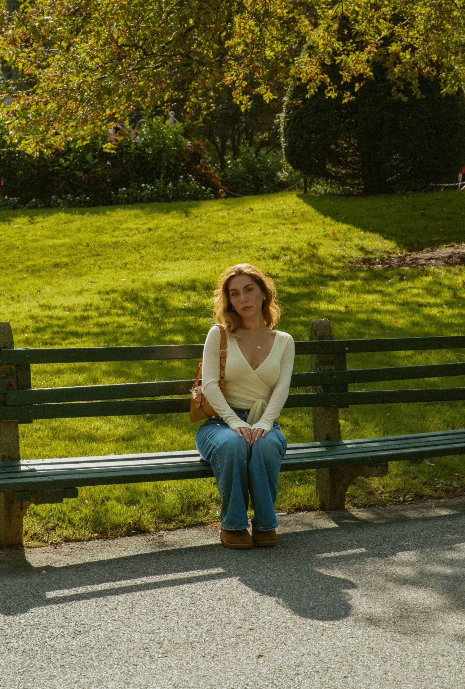 Person in white top and jeans sitting alone on park bench against green landscape.