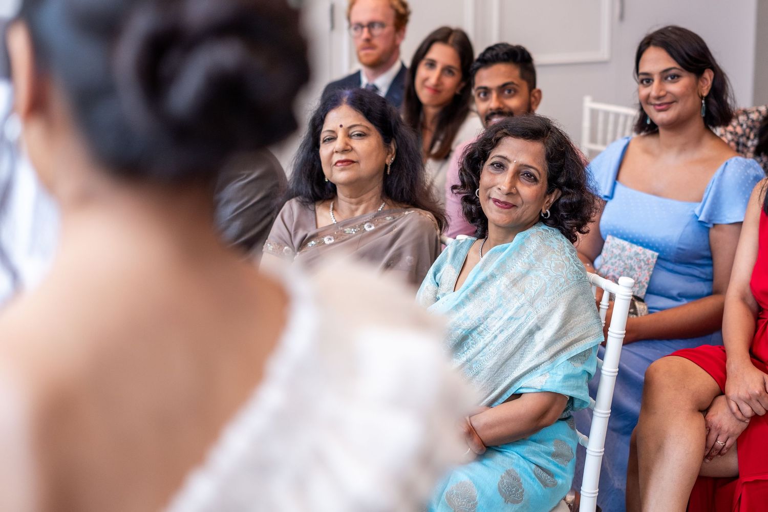 Guests smiling warmly at a bride during a wedding ceremony, wearing colorful traditional and formal attire.