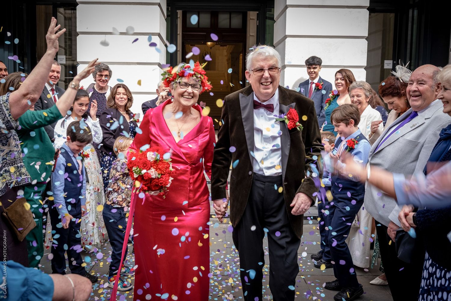 Elderly couple walking through confetti shower at wedding celebration outdoors.