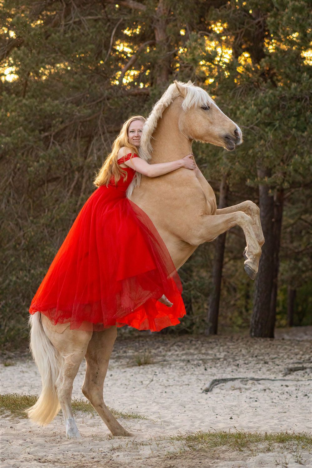 Vrouw in een rode jurk met een lichtbruin paard dat steigert.