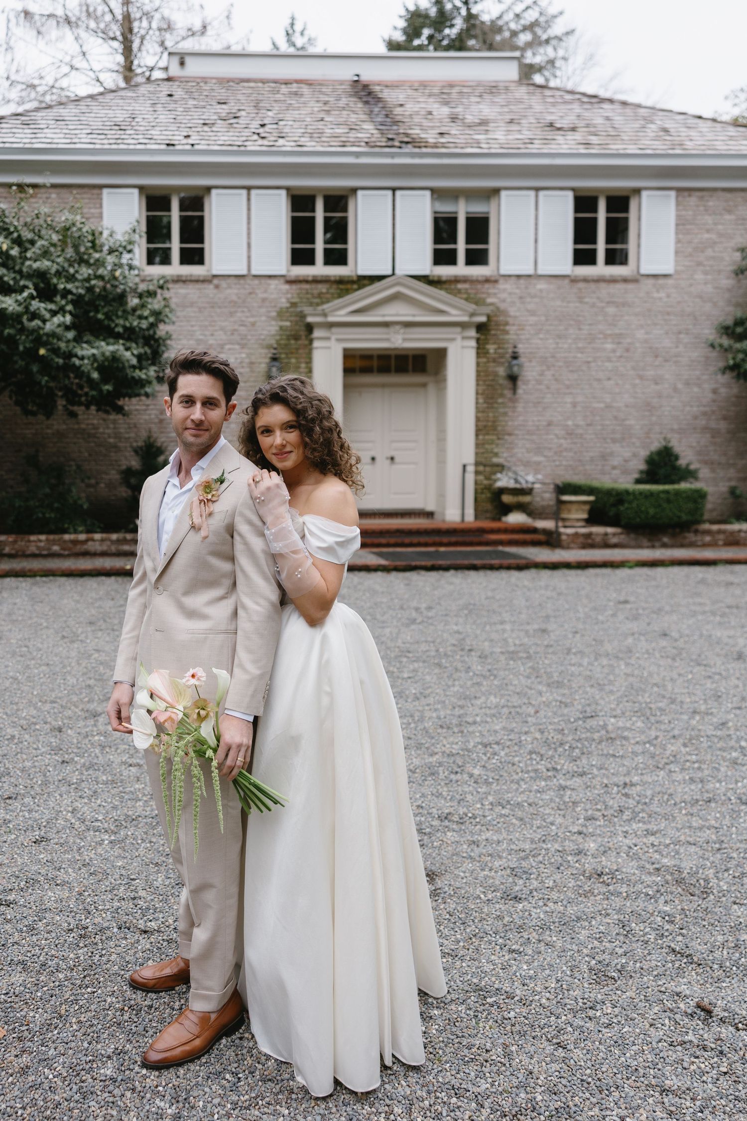 Bride and groom posing together in front of an elegant brick mansion on their wedding day.