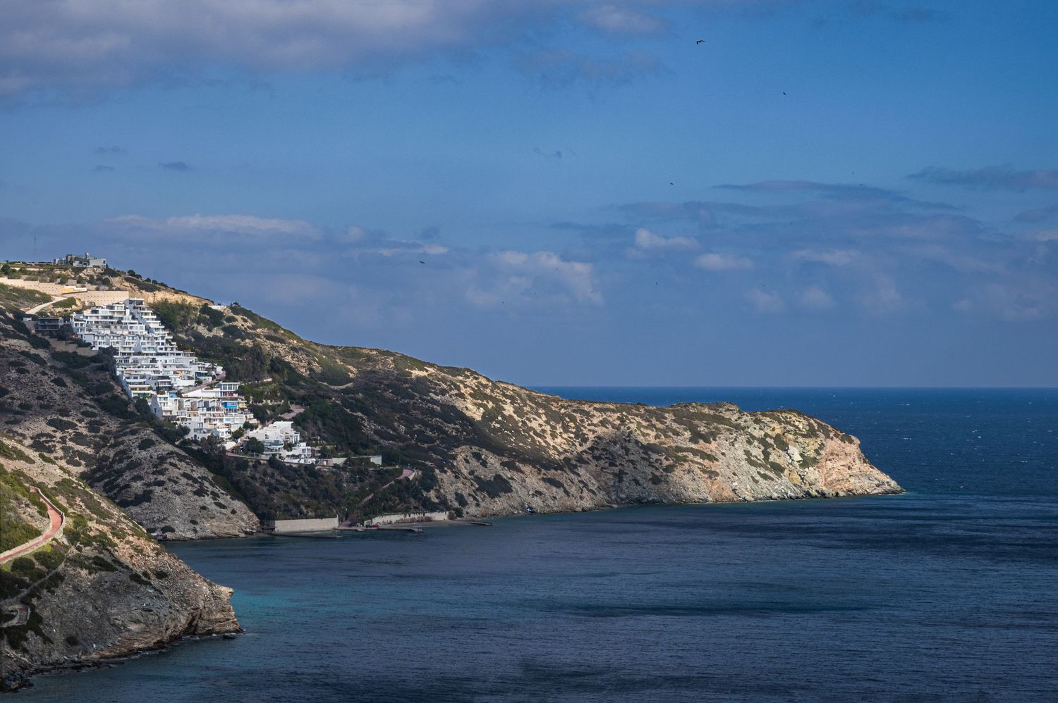 Panoramic view of rugged coastal cliffs and blue ocean waters stretching along a rocky shoreline under bright sky.