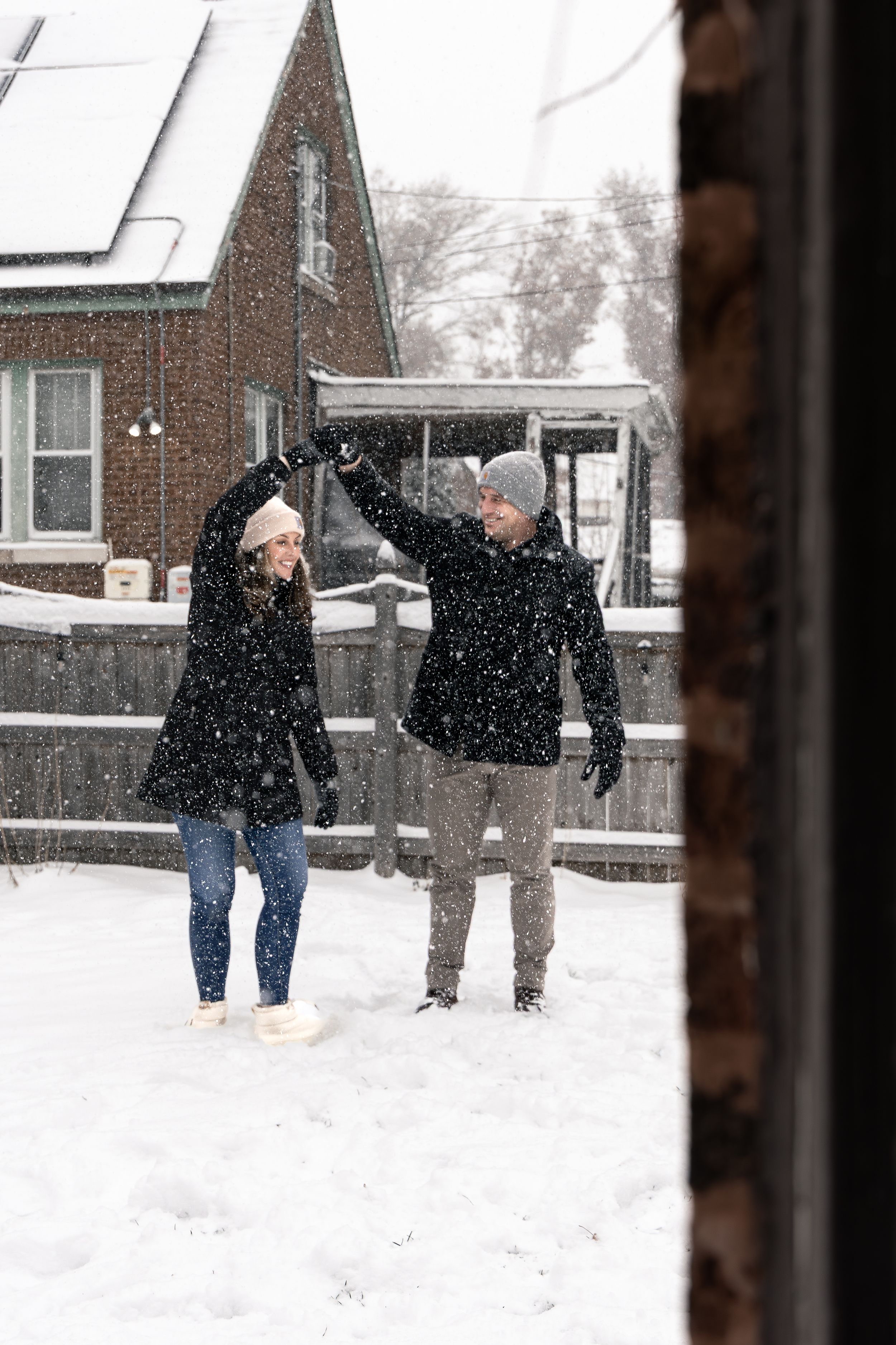 Two people playfully enjoying a snowy winter day outside a brick house.