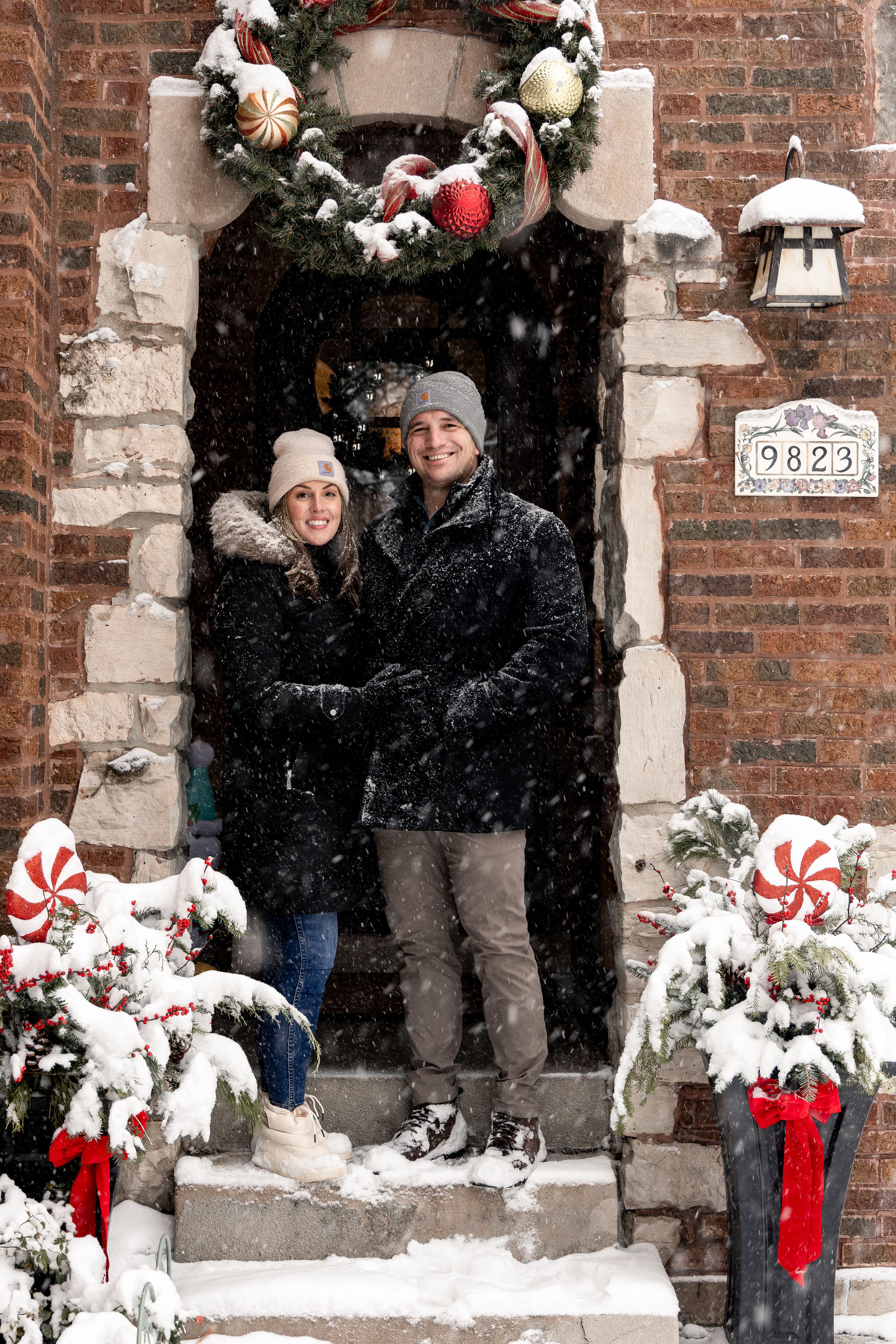 A playful winter scene shows people throwing snowballs between brick archways decorated with holiday ornaments and bows.