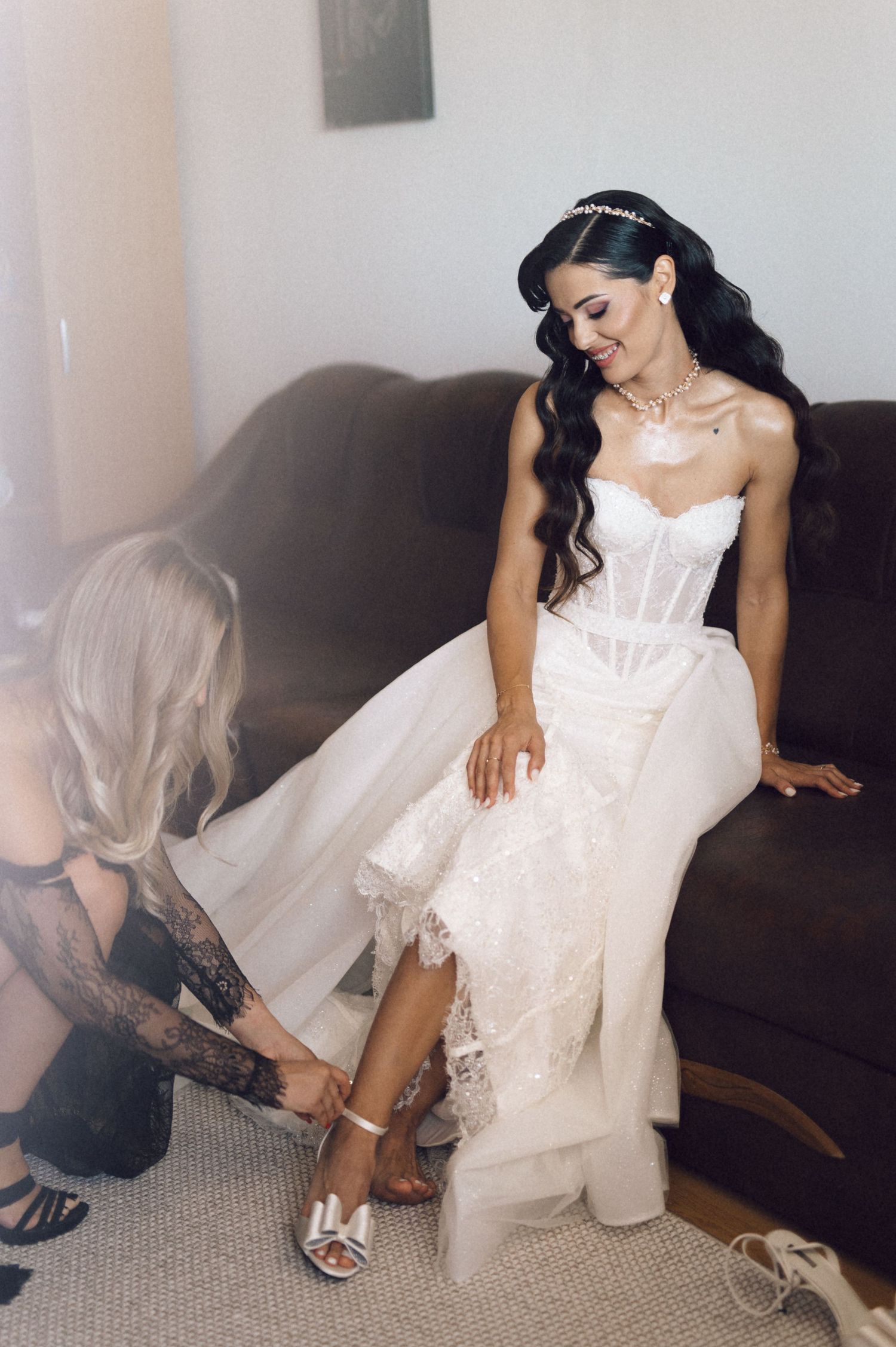 A person in a white dress sits on a dark couch in a series of graceful poses showing off their footwear.