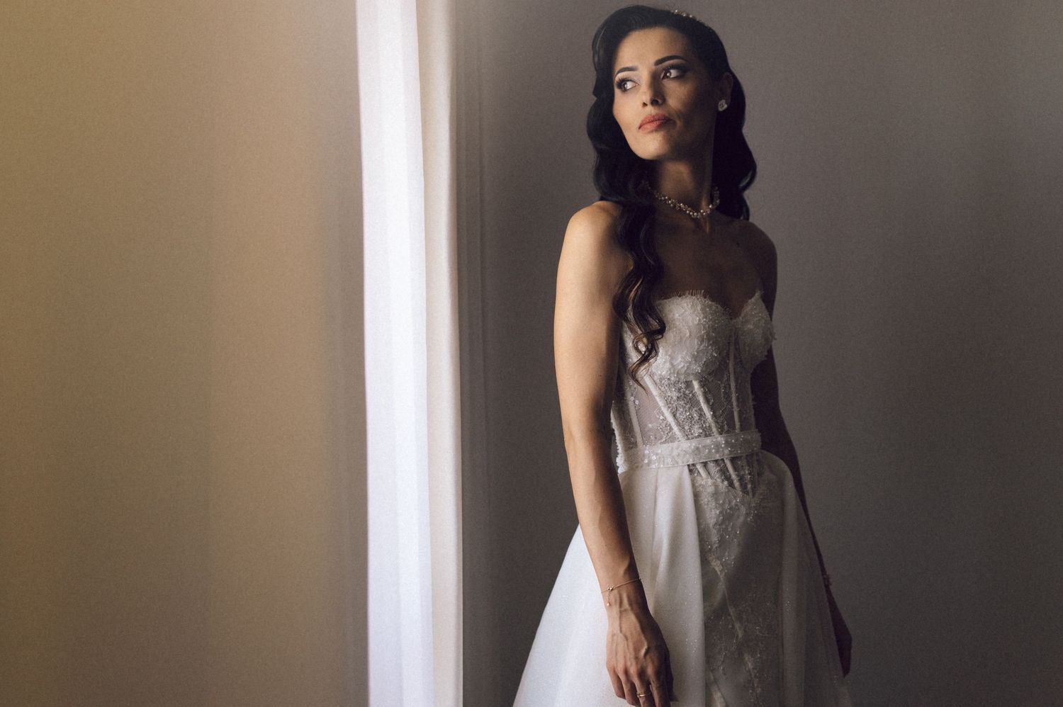 A person wearing a sleeveless gray dress poses against a light-colored wall in a fashion-style photoshoot.