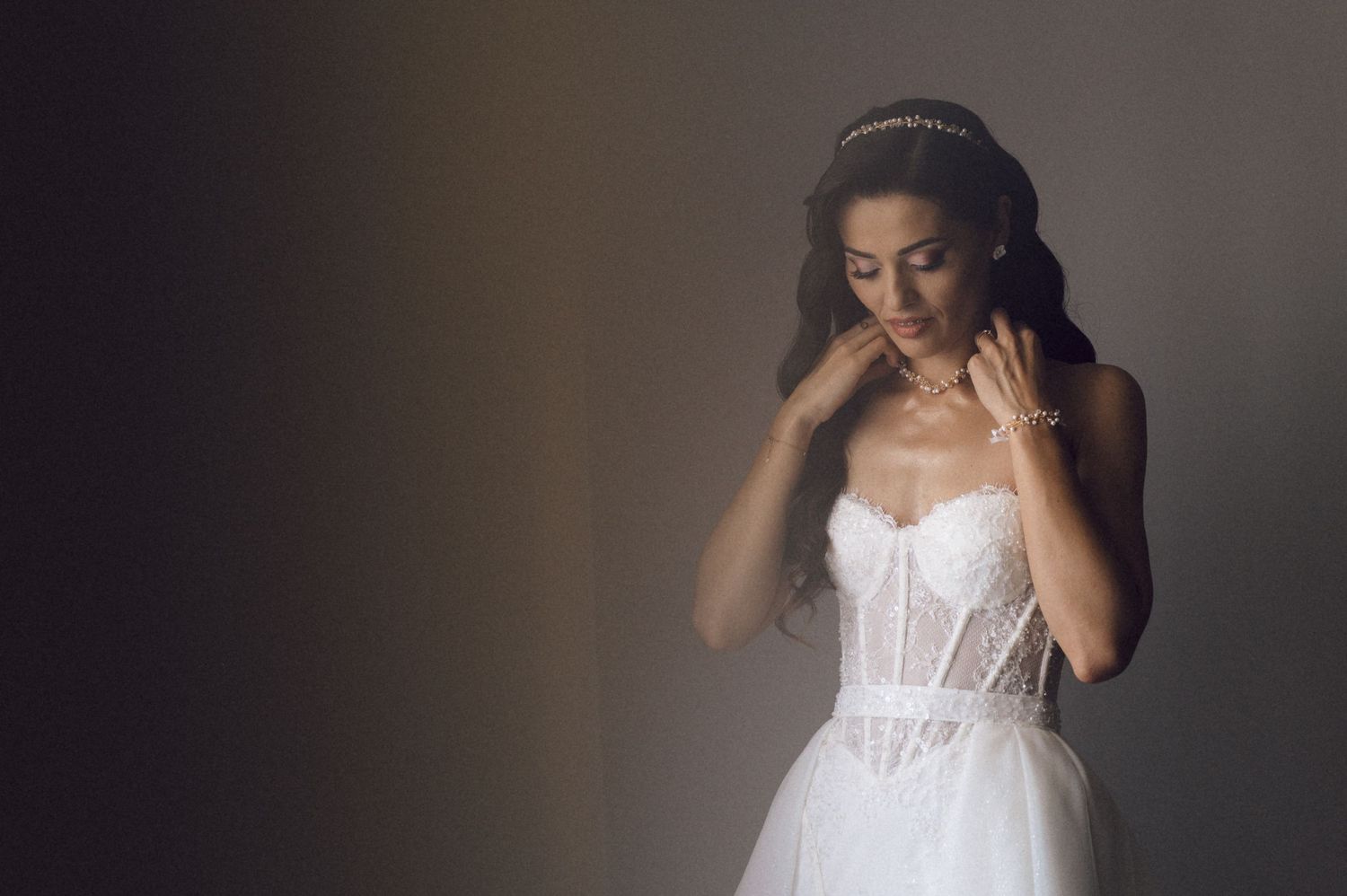 Bride wearing a flowing white corset wedding dress poses in dramatic lighting against a dark background.