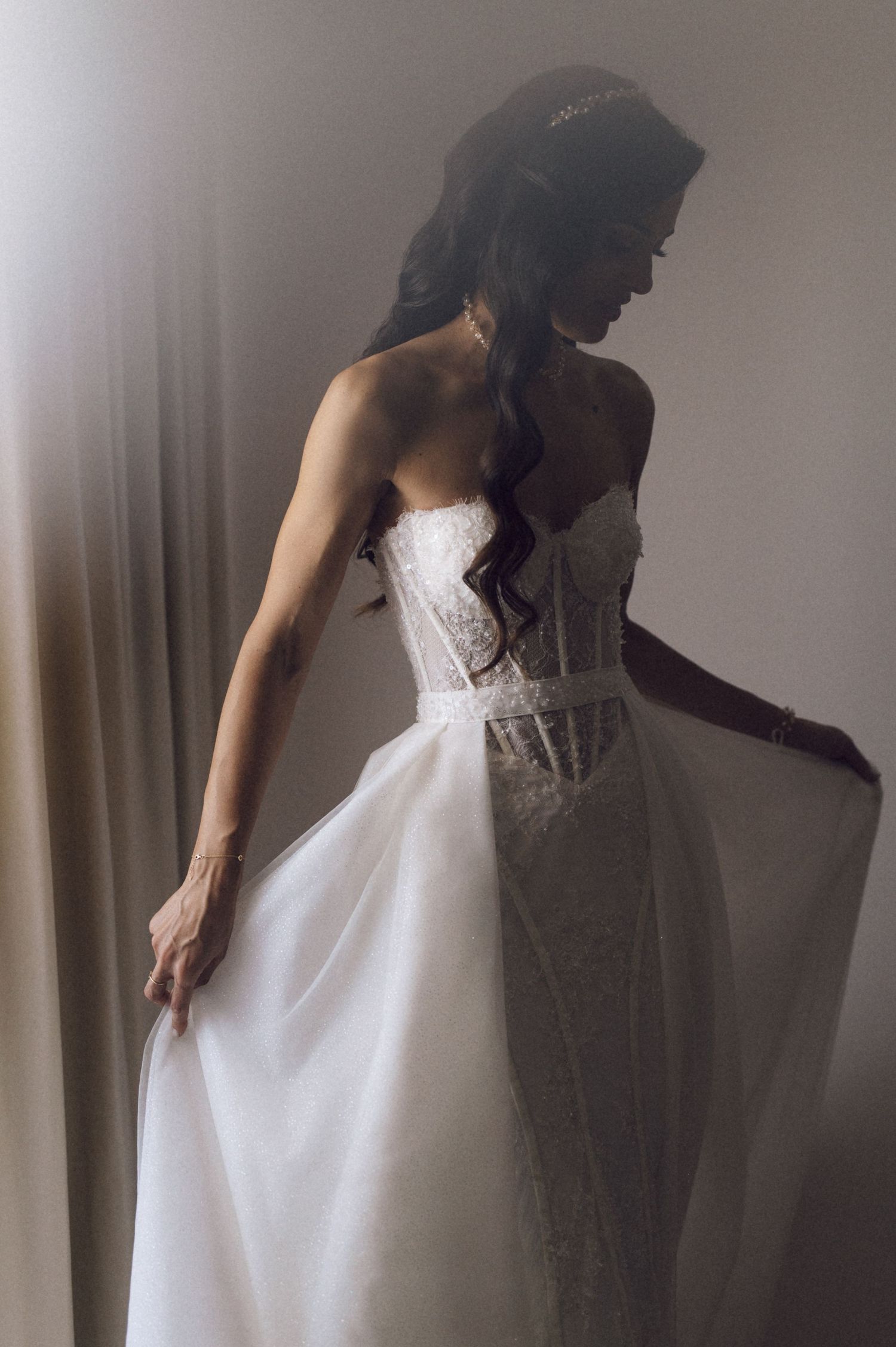 A silhouetted figure in a white wedding dress stands gracefully against a light background with flowing fabric details.