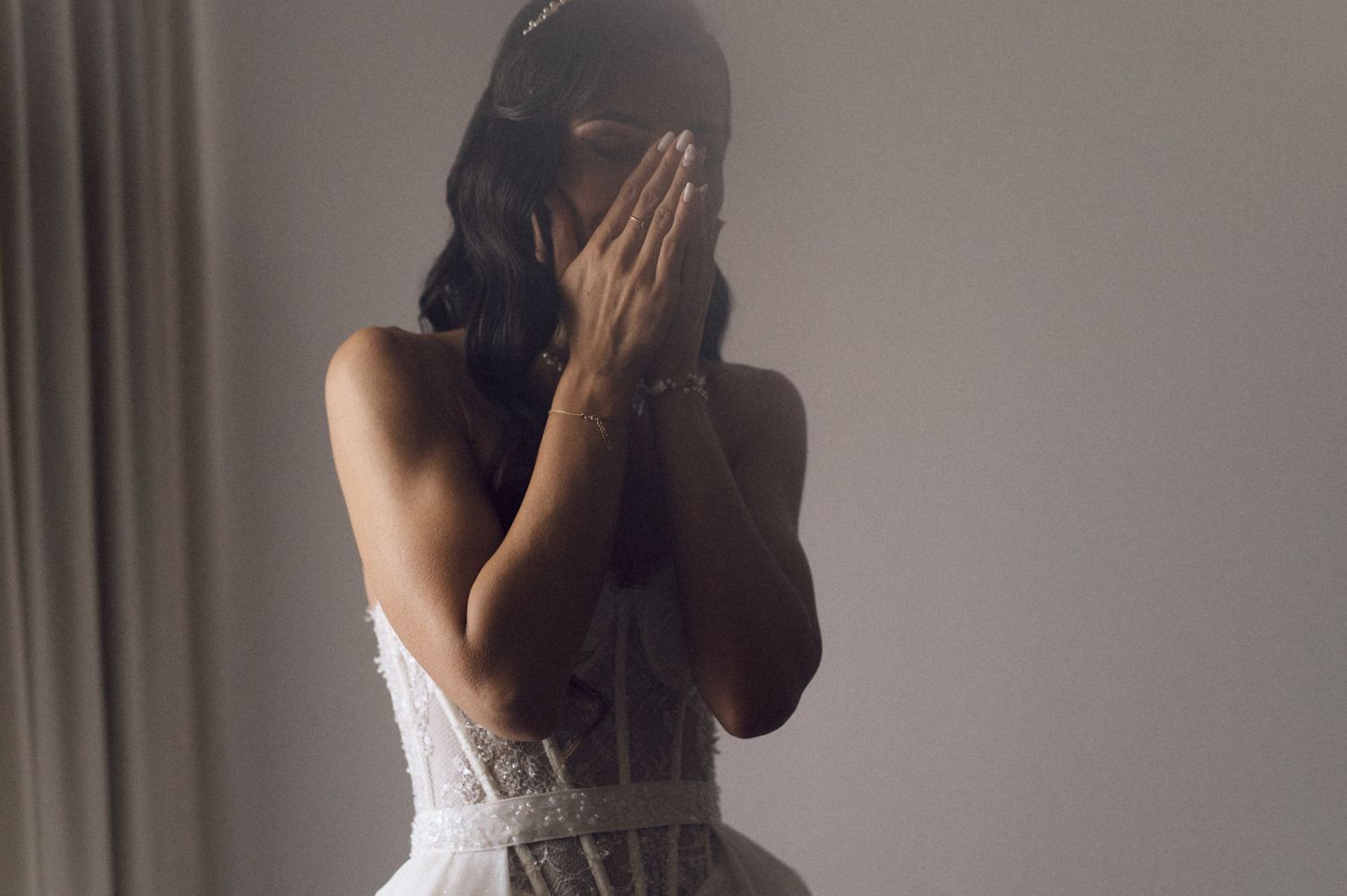 Woman in a white lace wedding dress with open back design stands in a romantic indoor setting.