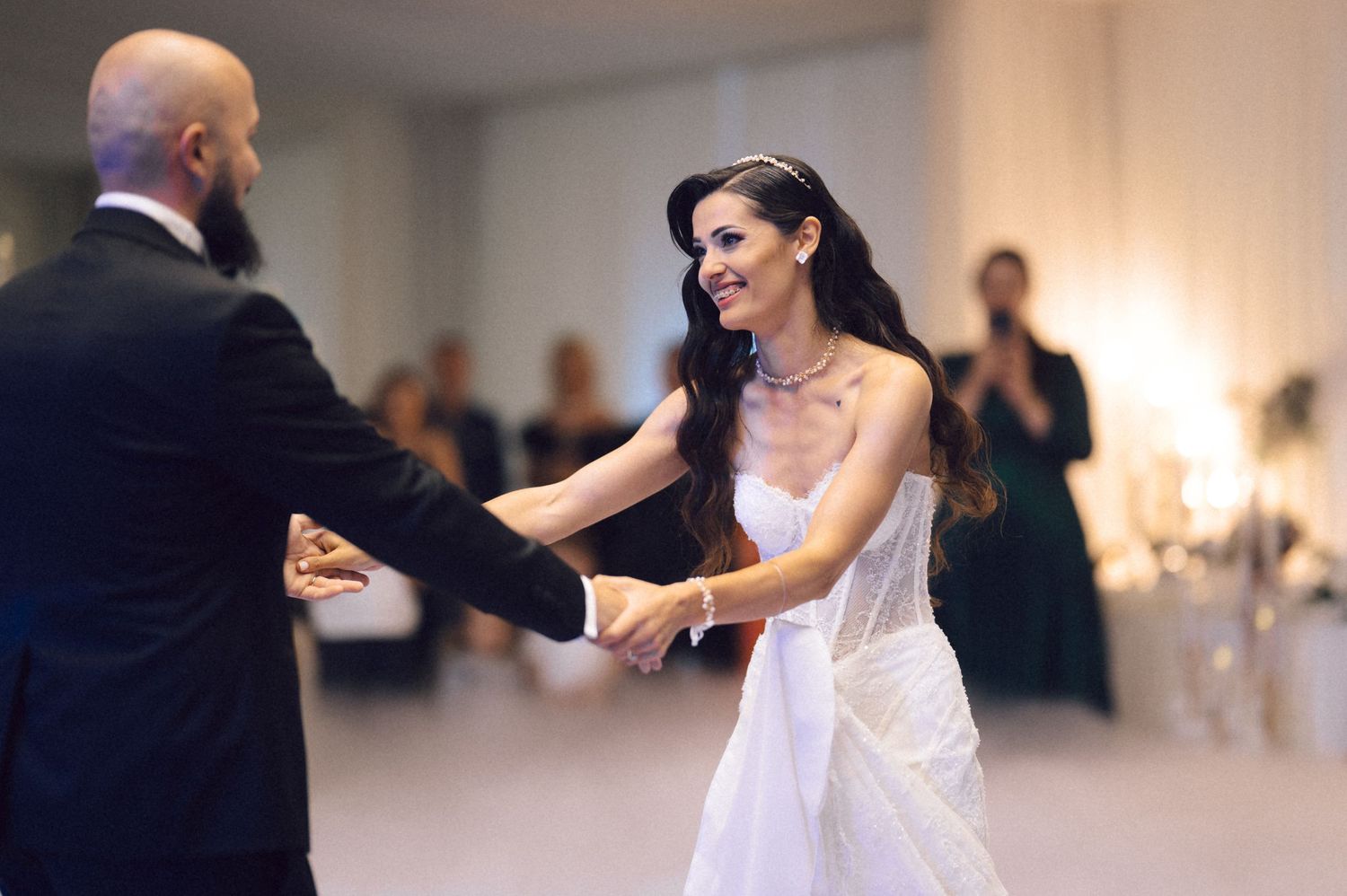 A bride in a white wedding gown dances with a bald man in a dark suit during their wedding reception.
