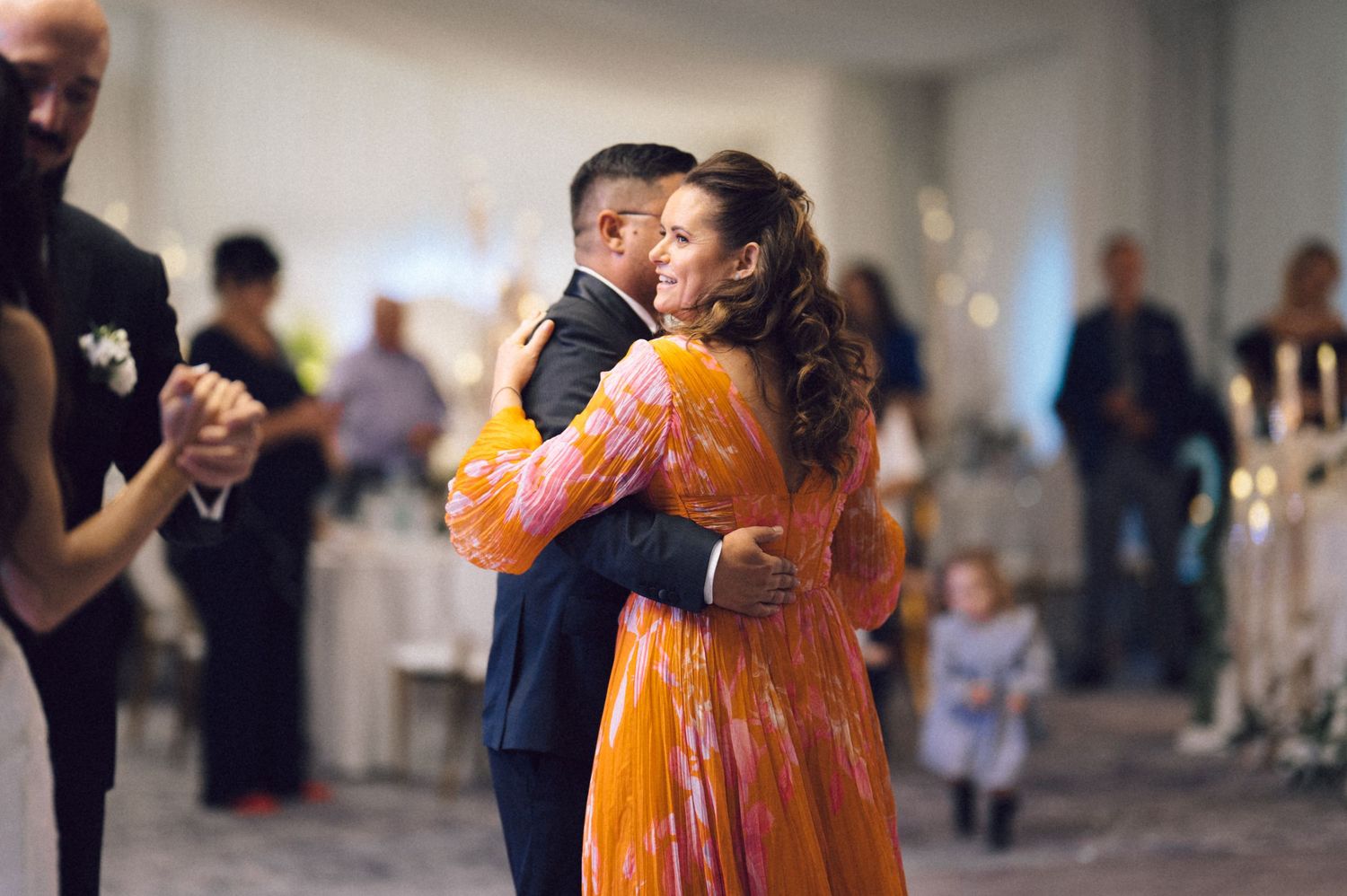 A couple in formal attire dances together at an elegant event with other guests visible in the background.