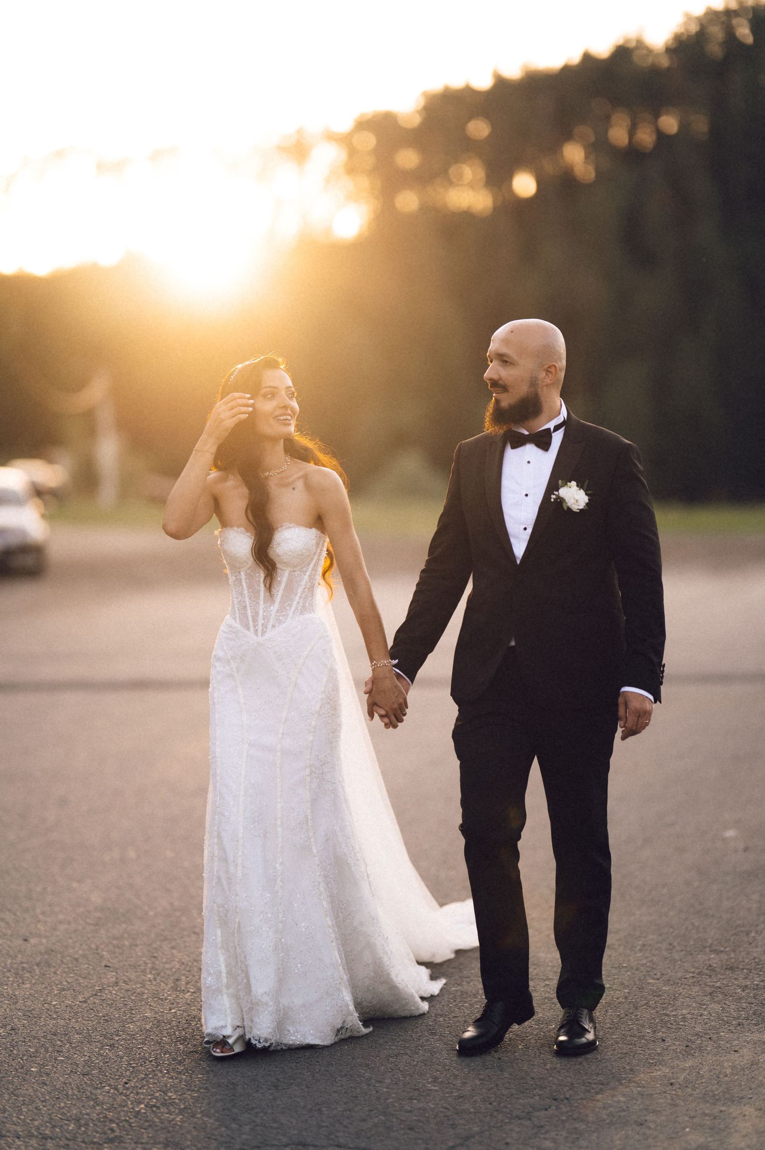 A newlywed couple walks together during golden hour sunset in formal wedding attire.