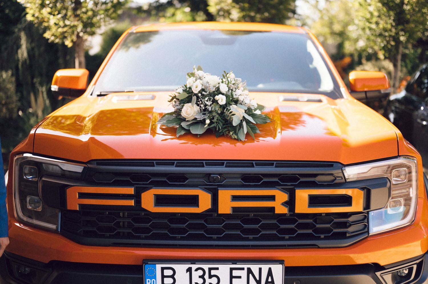 Orange Ford Bronco decorated with floral wedding arrangements parked outdoors.