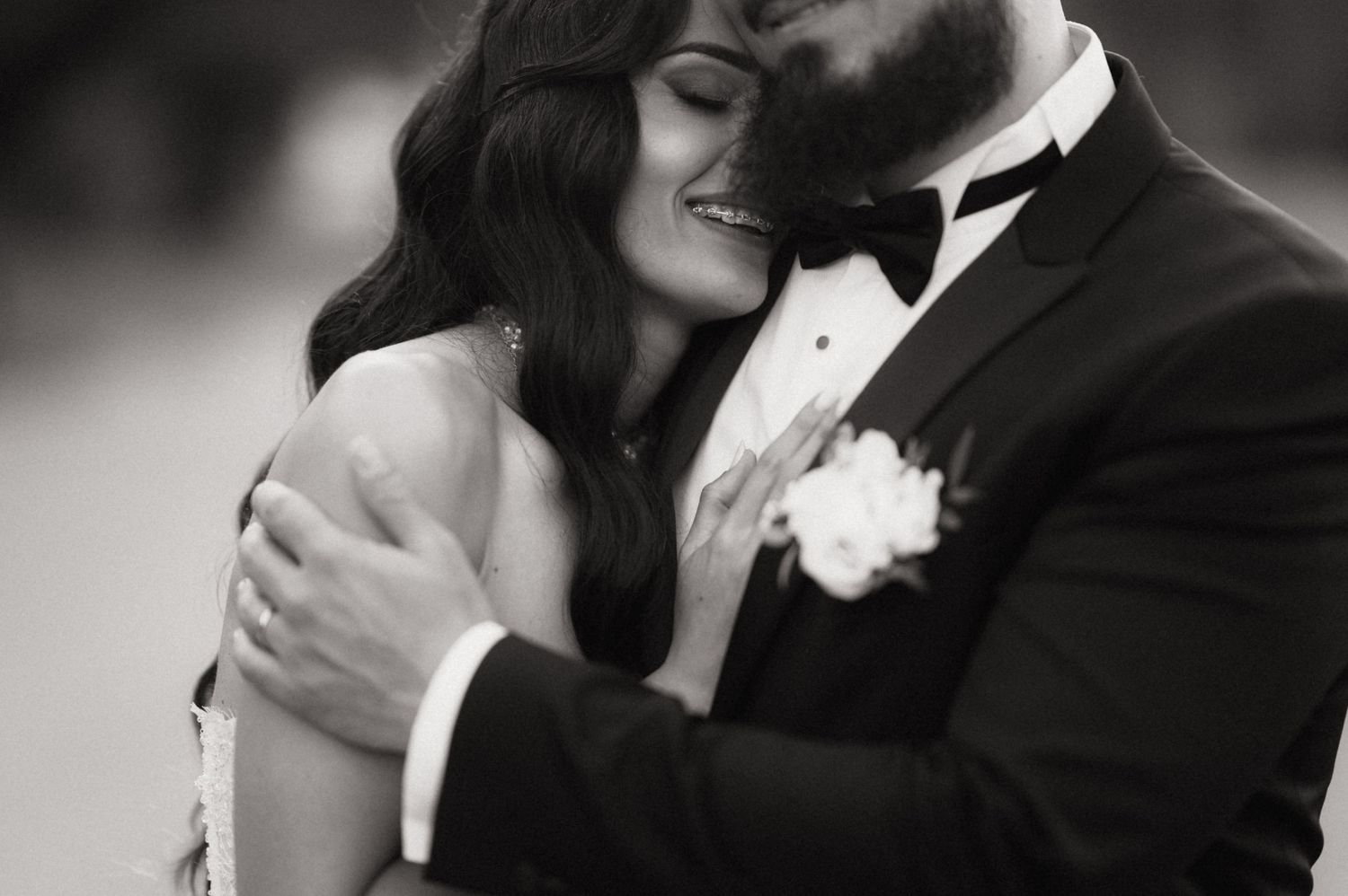 Black and white romantic wedding photo showing intimate embrace between couple, with groom in tuxedo and boutonniere.
