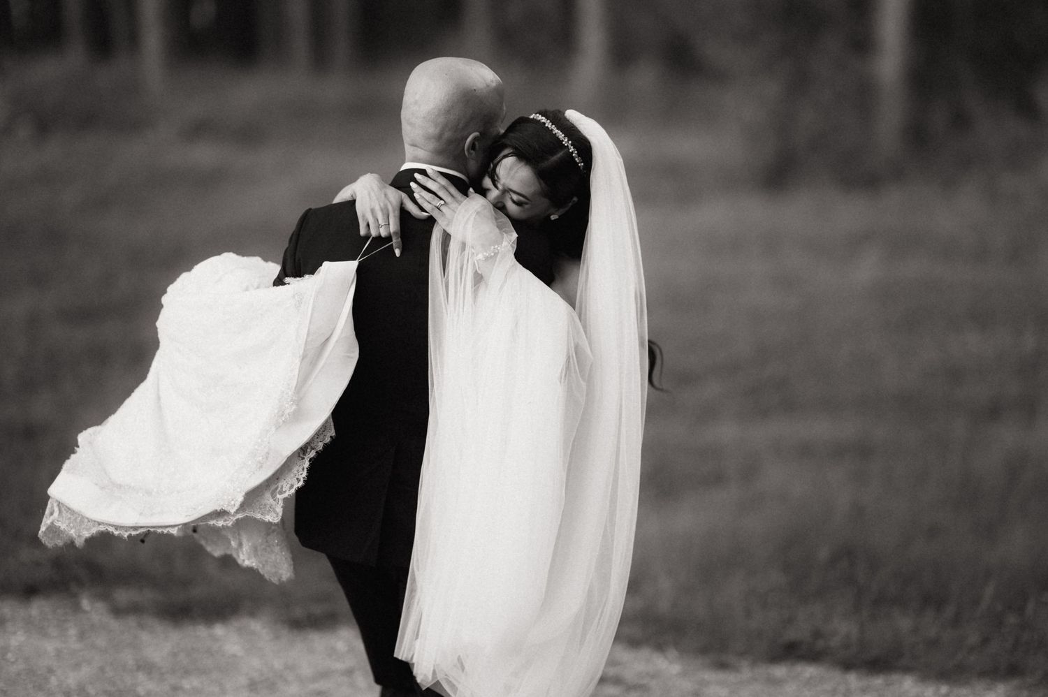 A couple in wedding attire share an intimate dance moment outdoors with flowing white dress fabric creating movement.