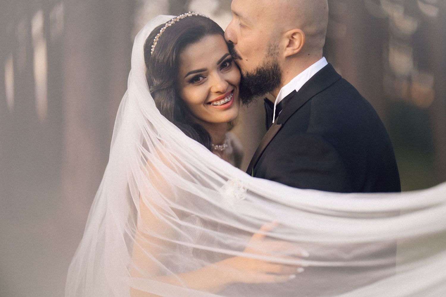 A romantic wedding couple embraces as the bride's veil flows gracefully in the breeze during their outdoor photo session.