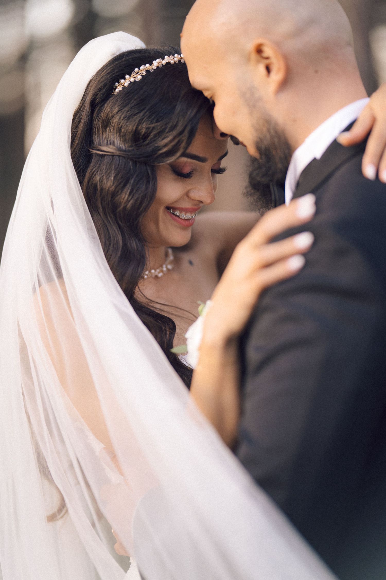 A tender moment between newlyweds as they embrace, with the bride wearing a delicate veil and crystal headpiece.