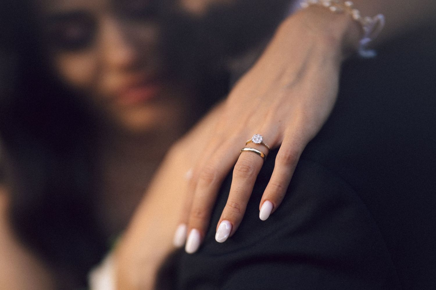 Close-up shot of elegant hands with white manicured nails and a sparkling diamond engagement ring.
