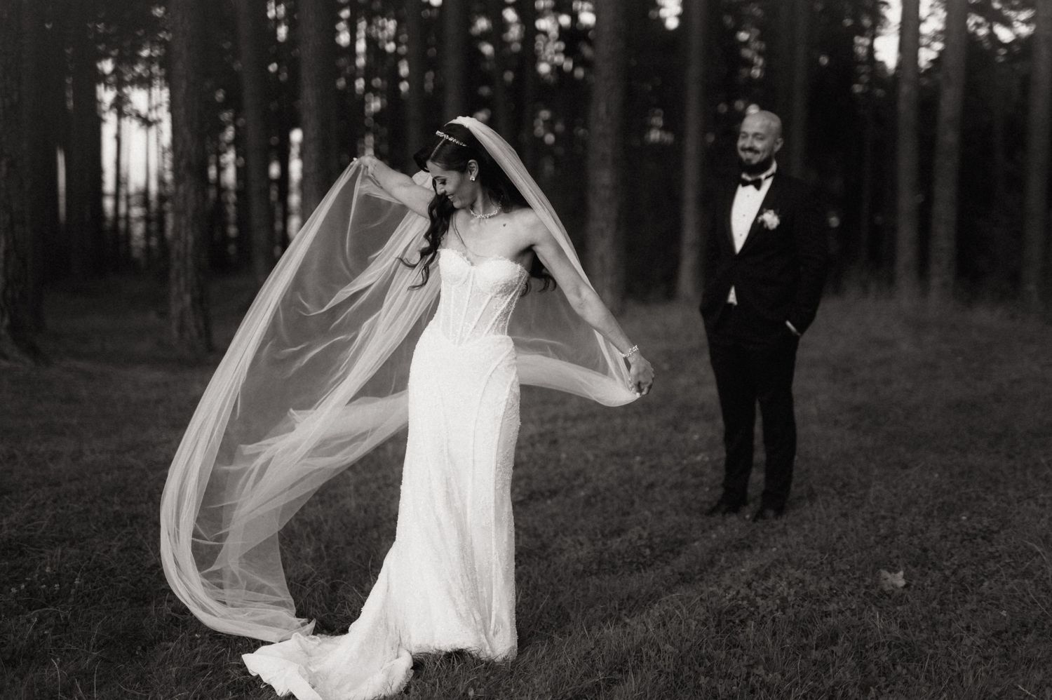 A bride and groom walk through a serene forest setting as her veil flows elegantly in the wind.