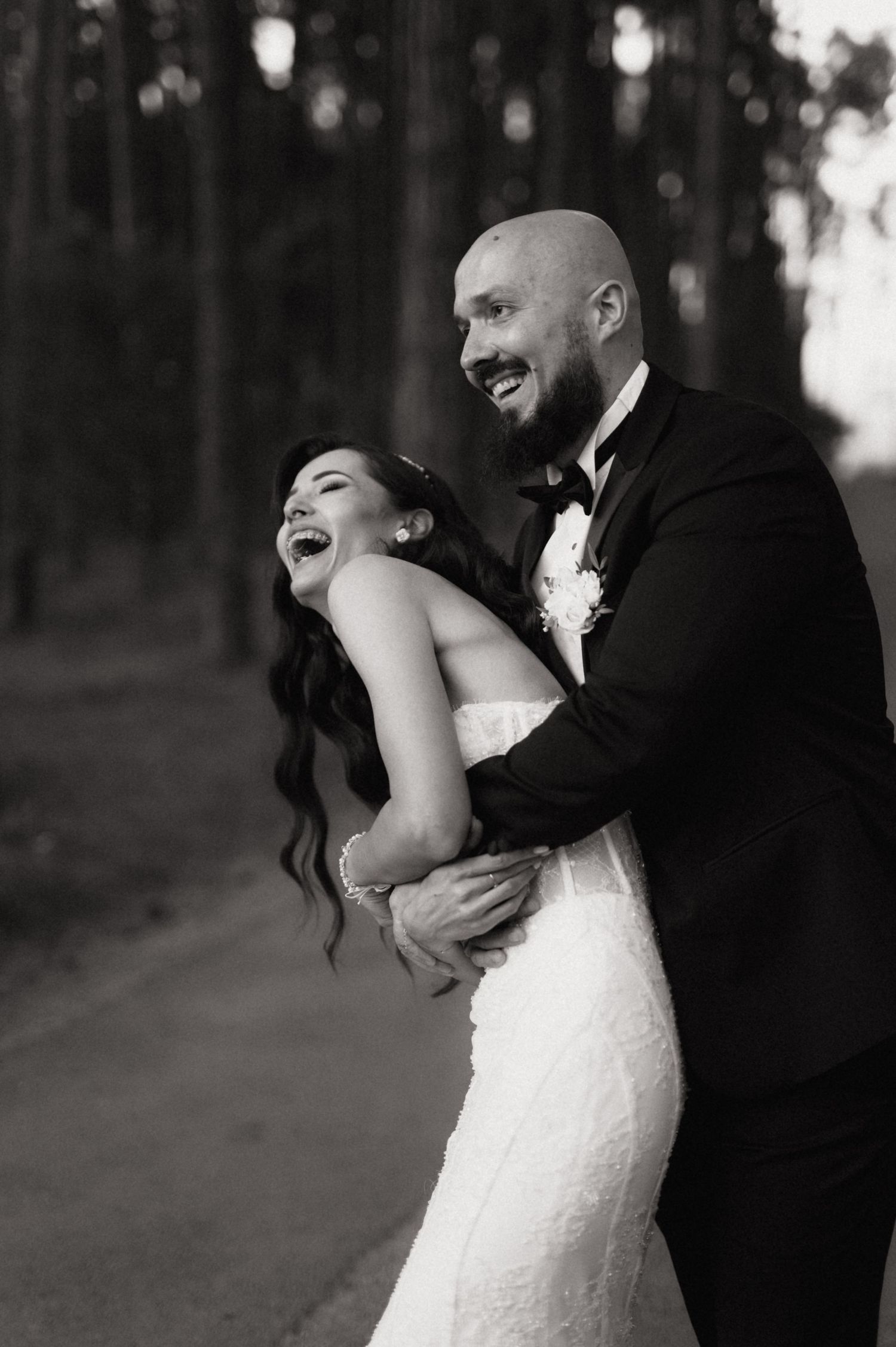 A romantic black and white wedding photo series showing a couple dancing and laughing together in a wooded setting.