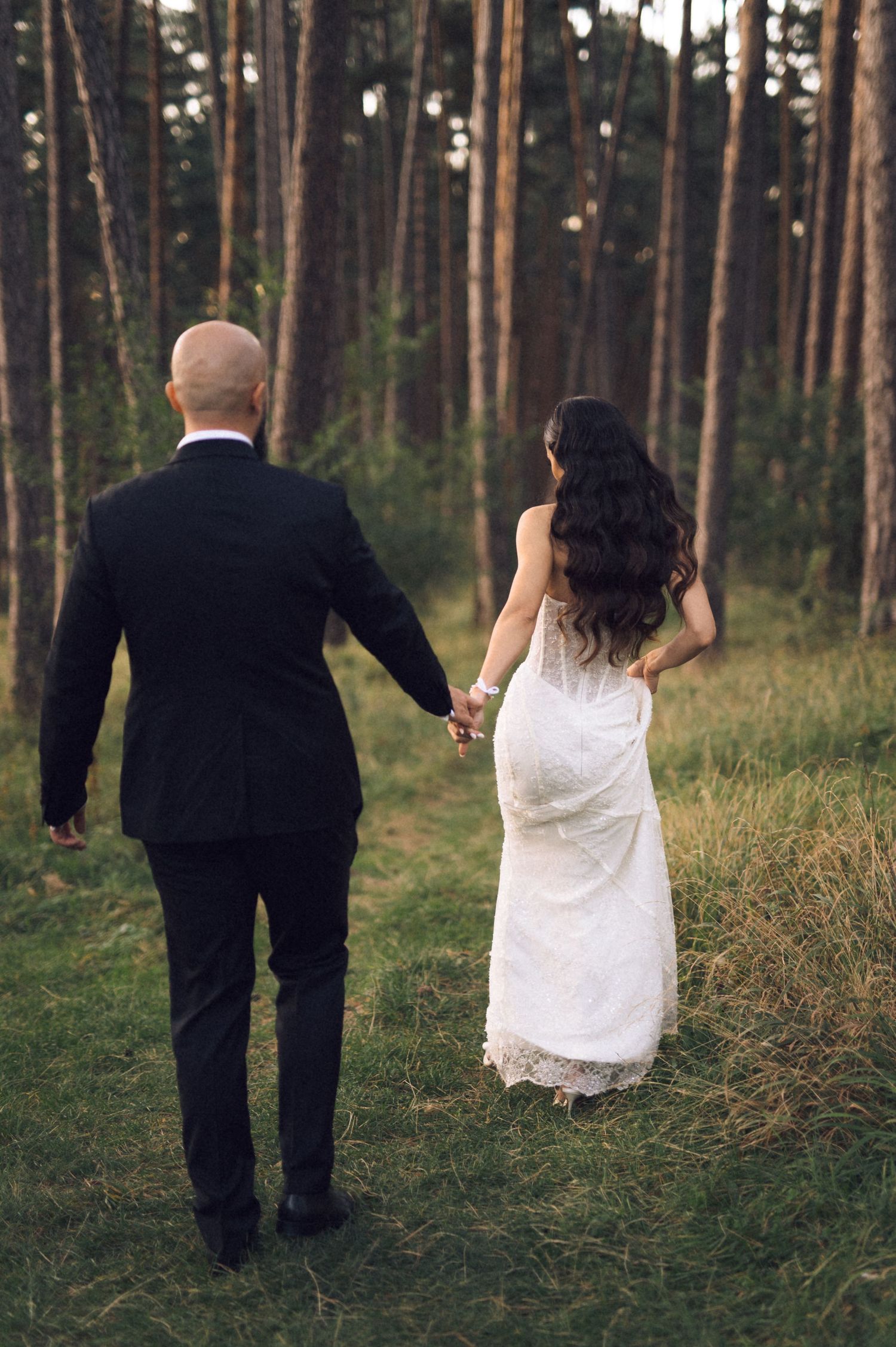 A couple in wedding attire walking through a serene pine forest, captured in a series of artistic back view shots.