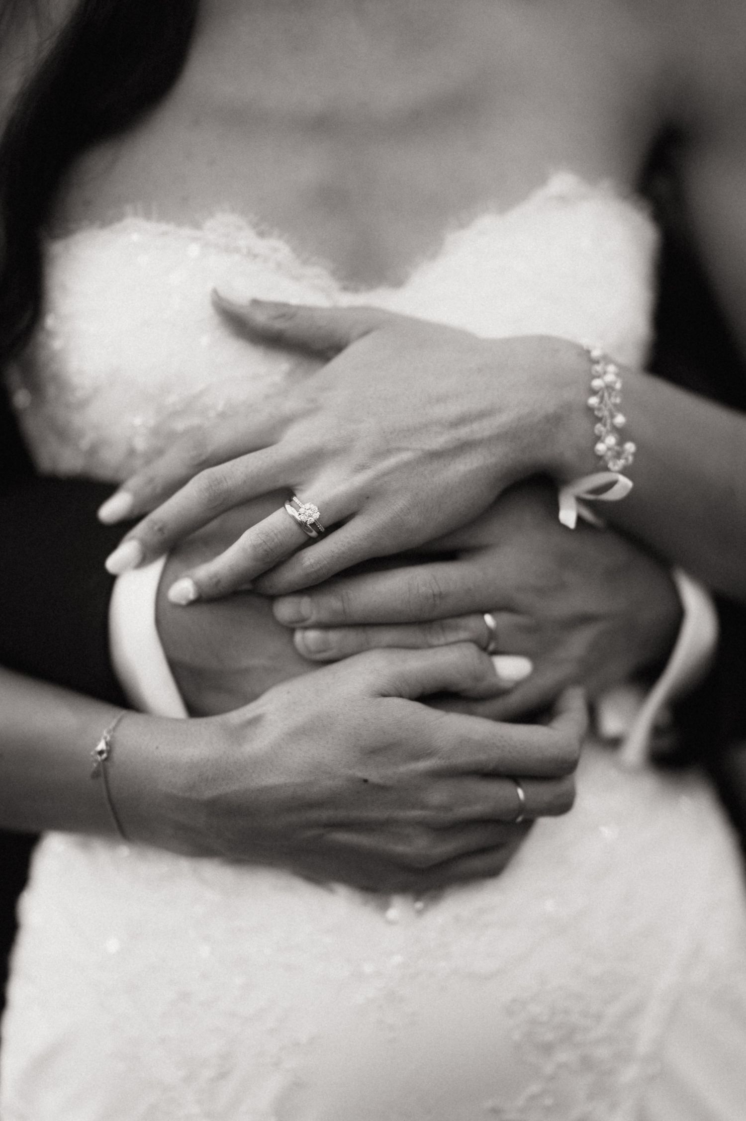 A series of black and white photos showing hands with wedding rings in various intimate poses against a white dress.