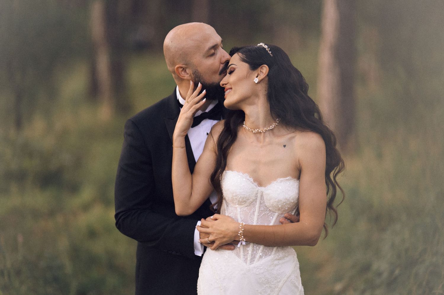 Romantic couple in wedding attire sharing an intimate moment in a dreamy outdoor setting with soft natural lighting.