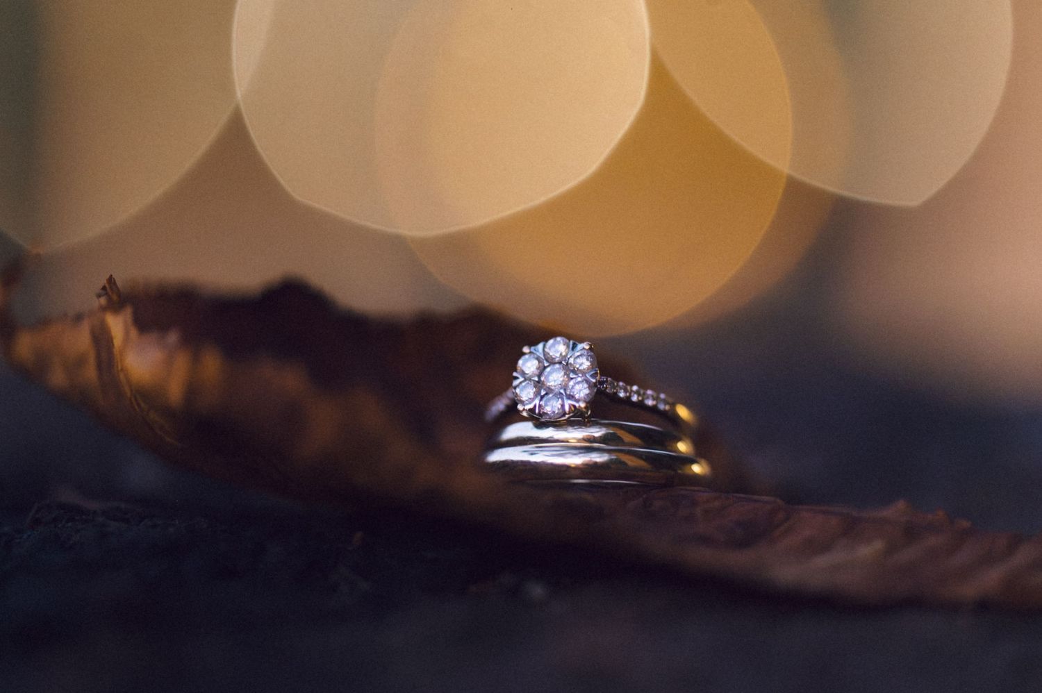Wedding rings displayed on a dark surface with soft bokeh lighting effects in the background.