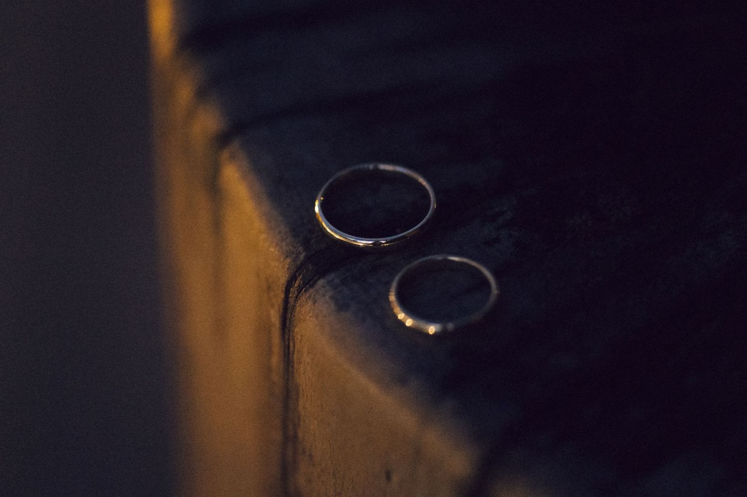 Seven identical wedding rings lined up in a row on a dark surface with warm lighting.
