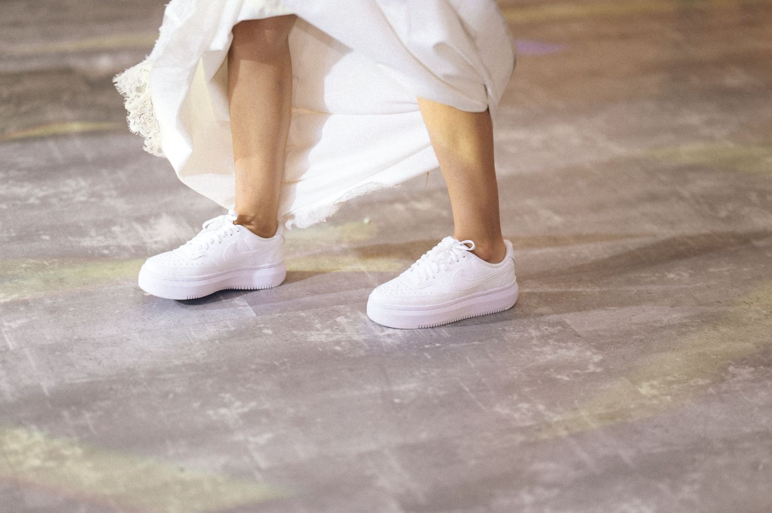 A close-up view of white sneakers on a wooden floor shows multiple angles and positions of the footwear.
