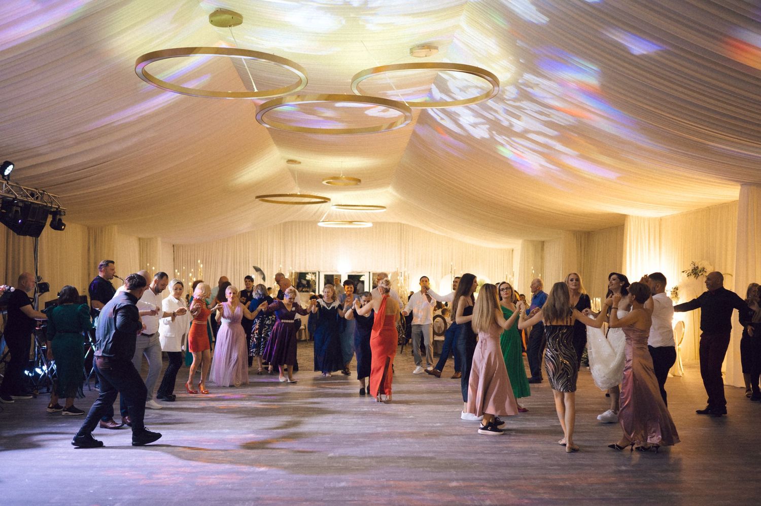 Couples dancing together in an elegant ballroom with white draped ceiling and warm lighting.