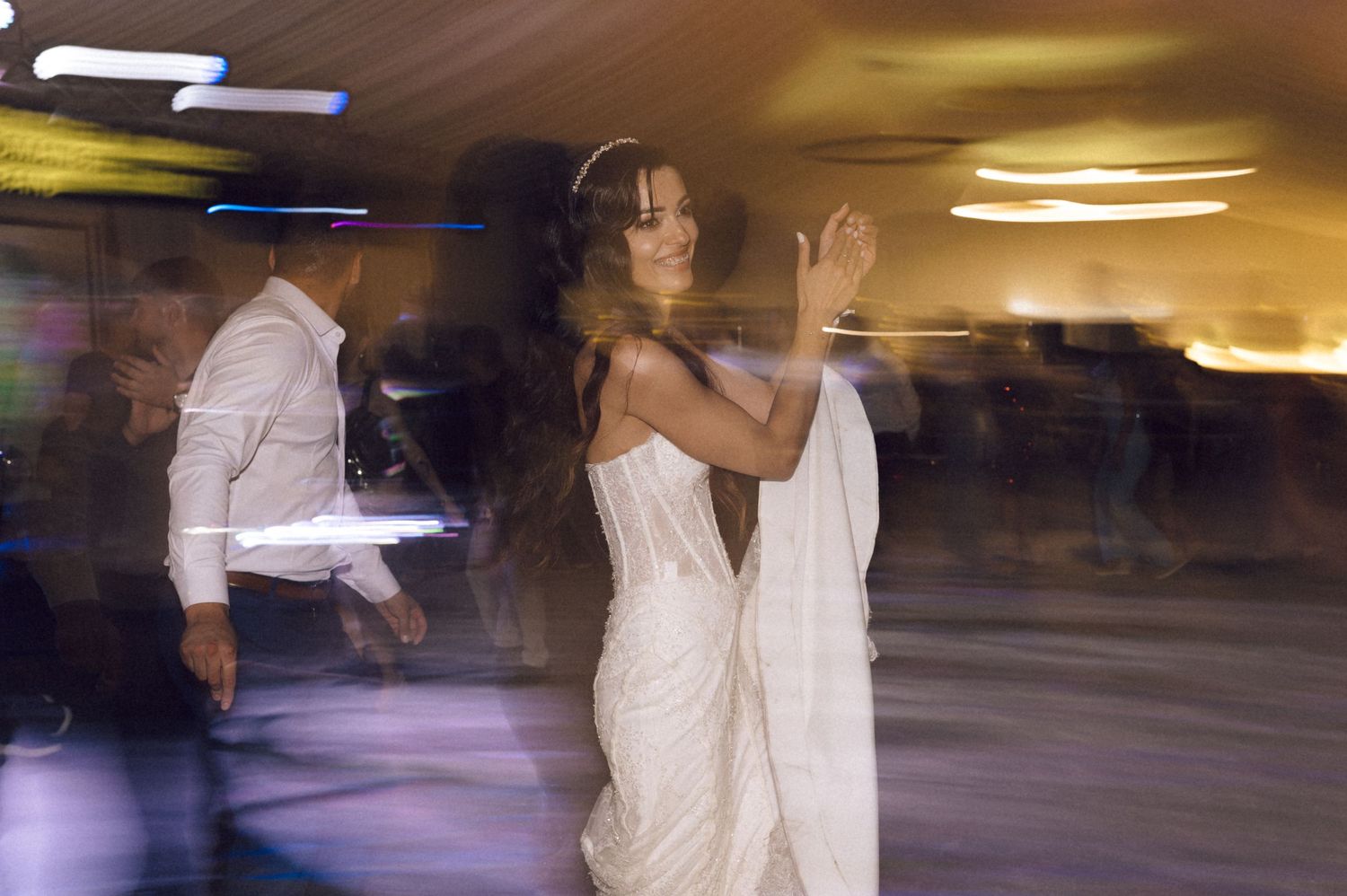 Motion-blurred dance sequence shows figures in white formal attire twirling across a dimly lit ballroom floor.