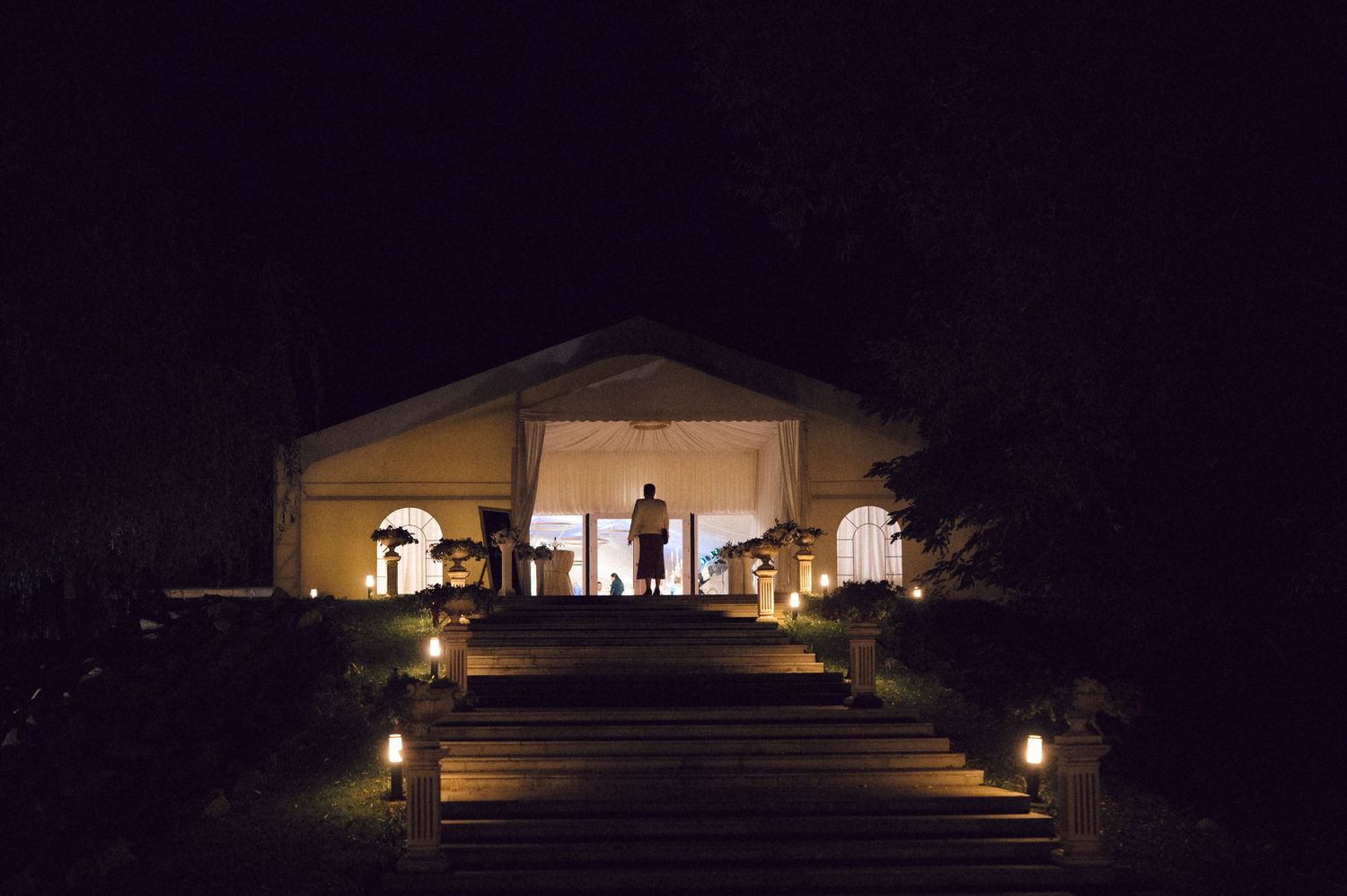 A modern house illuminated at night with warm lighting visible through large windows and glass doors.