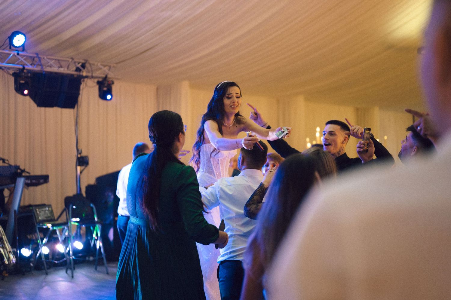 People dancing and celebrating at a wedding reception in a white tent with blue lighting effects.