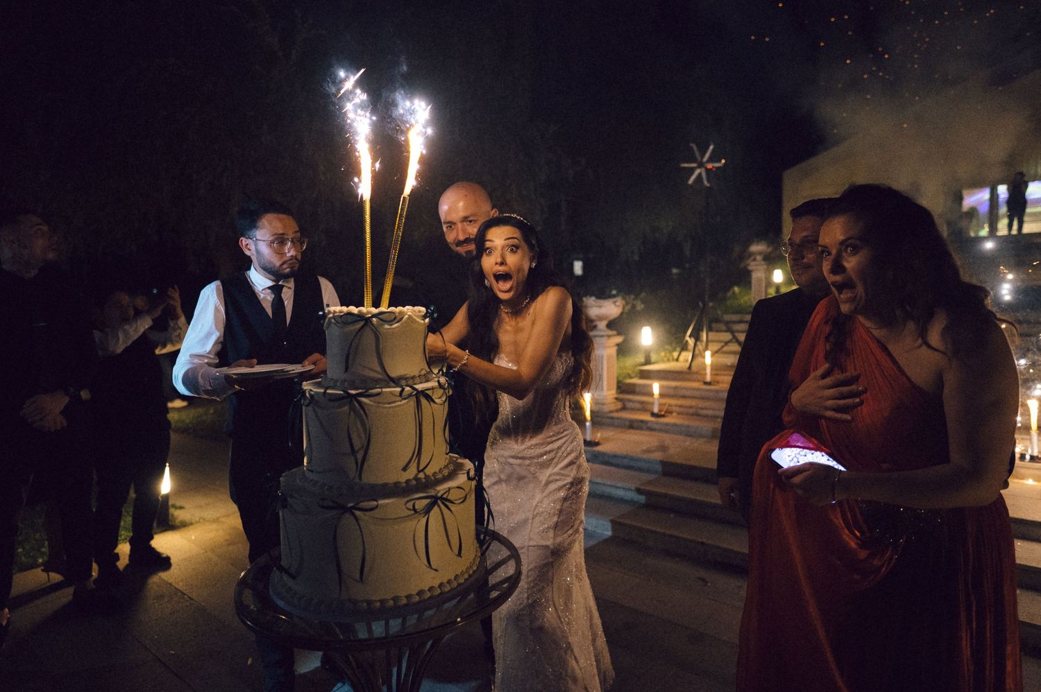 People gather outdoors at night holding sparklers and celebrating during a festive evening event.
