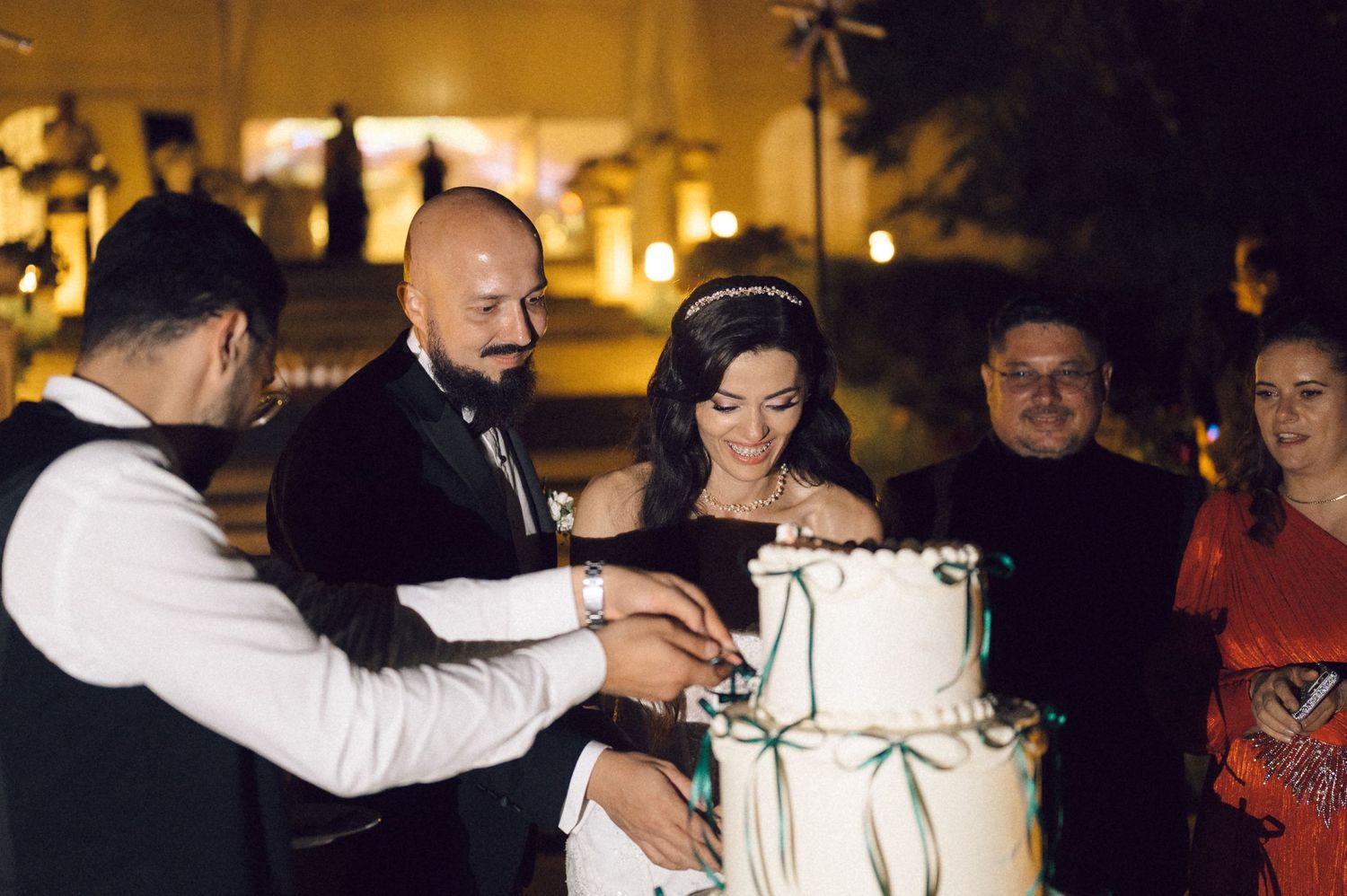 Wedding guests gather around a beautifully lit reception area at night with warm ambient lighting.