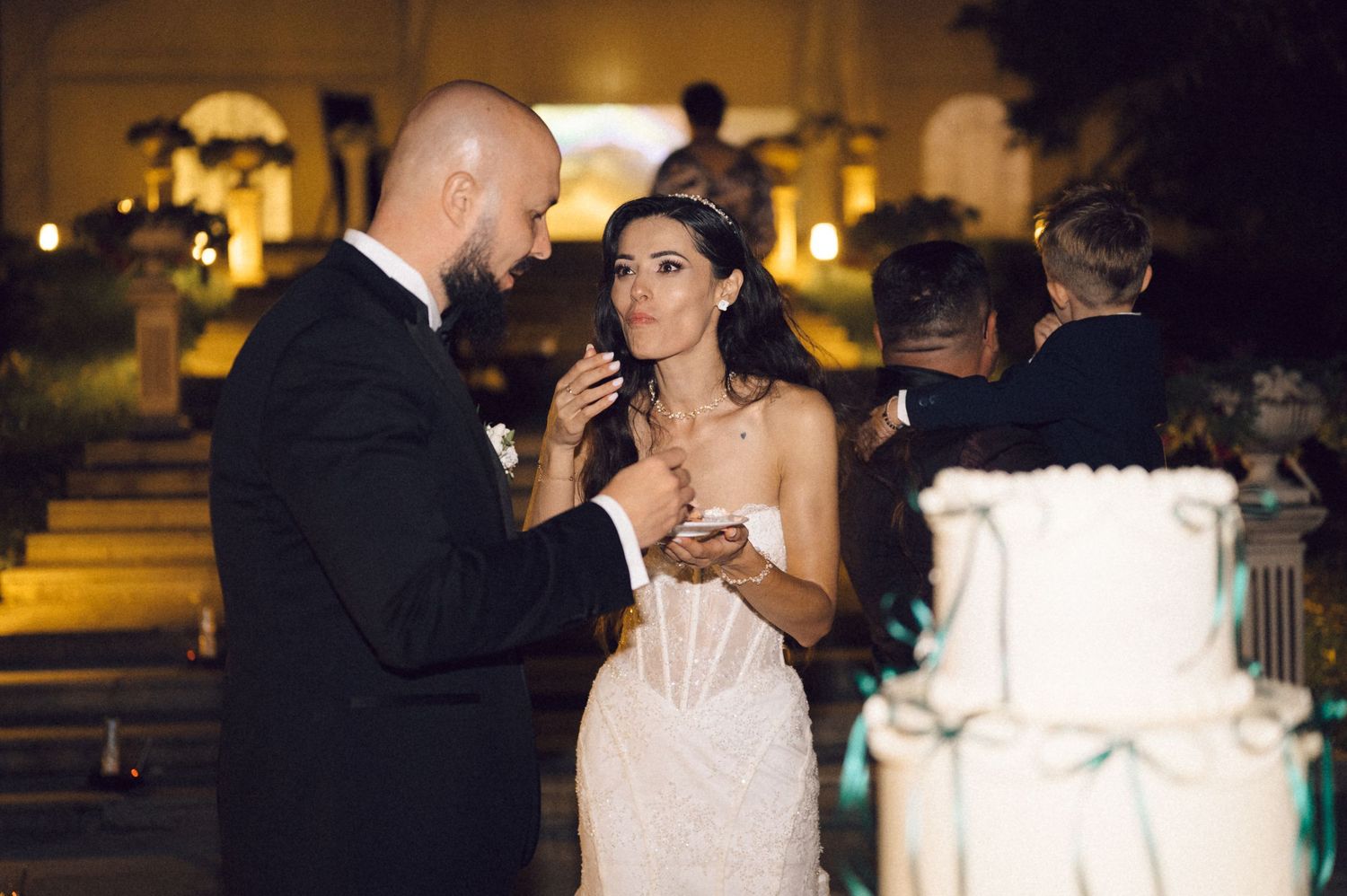 A couple shares a romantic dance moment during their wedding reception at night with glowing lights in the background.