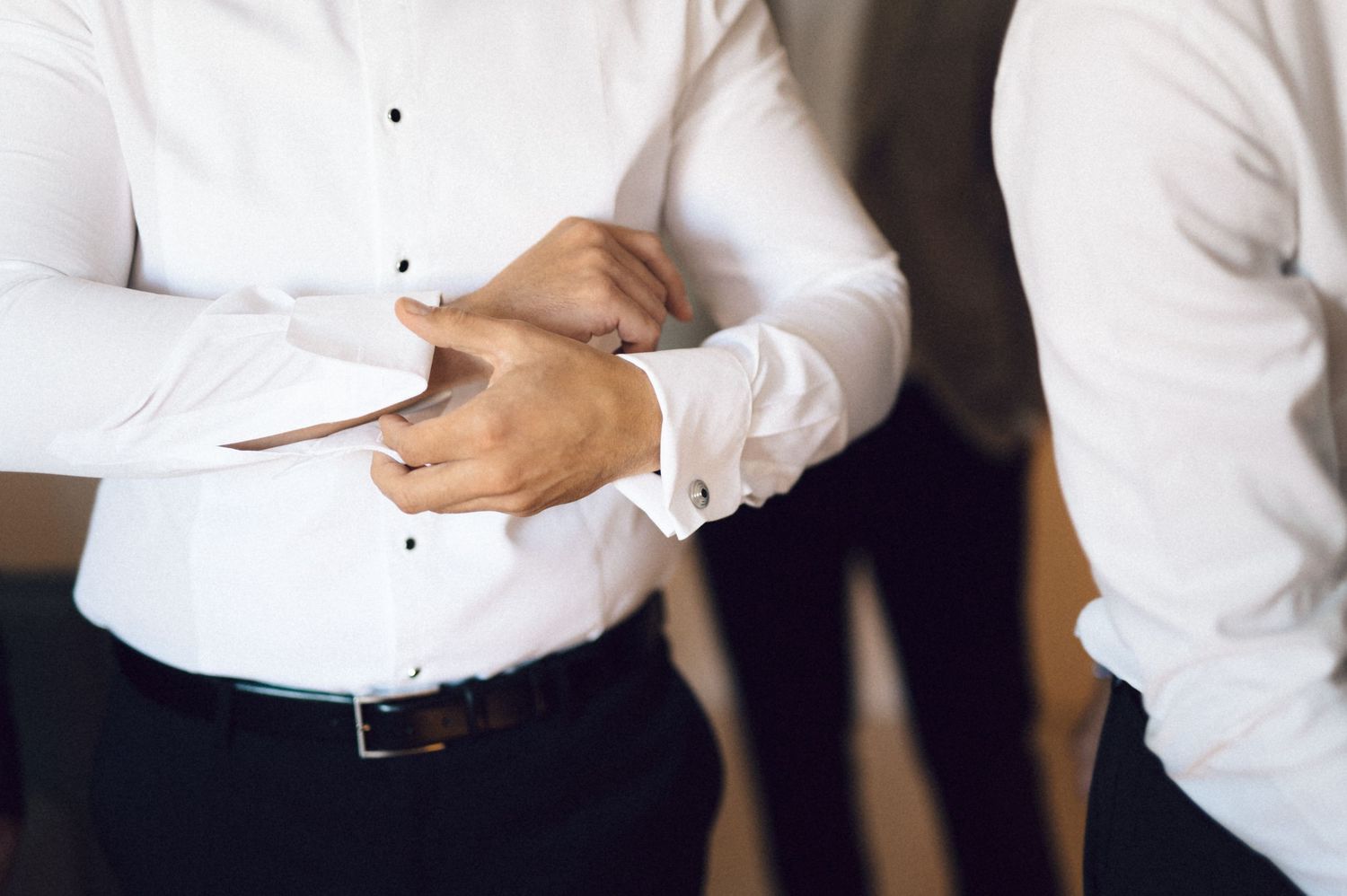 Professional in a white button-down shirt stands with arms crossed while holding documents in an office setting.
