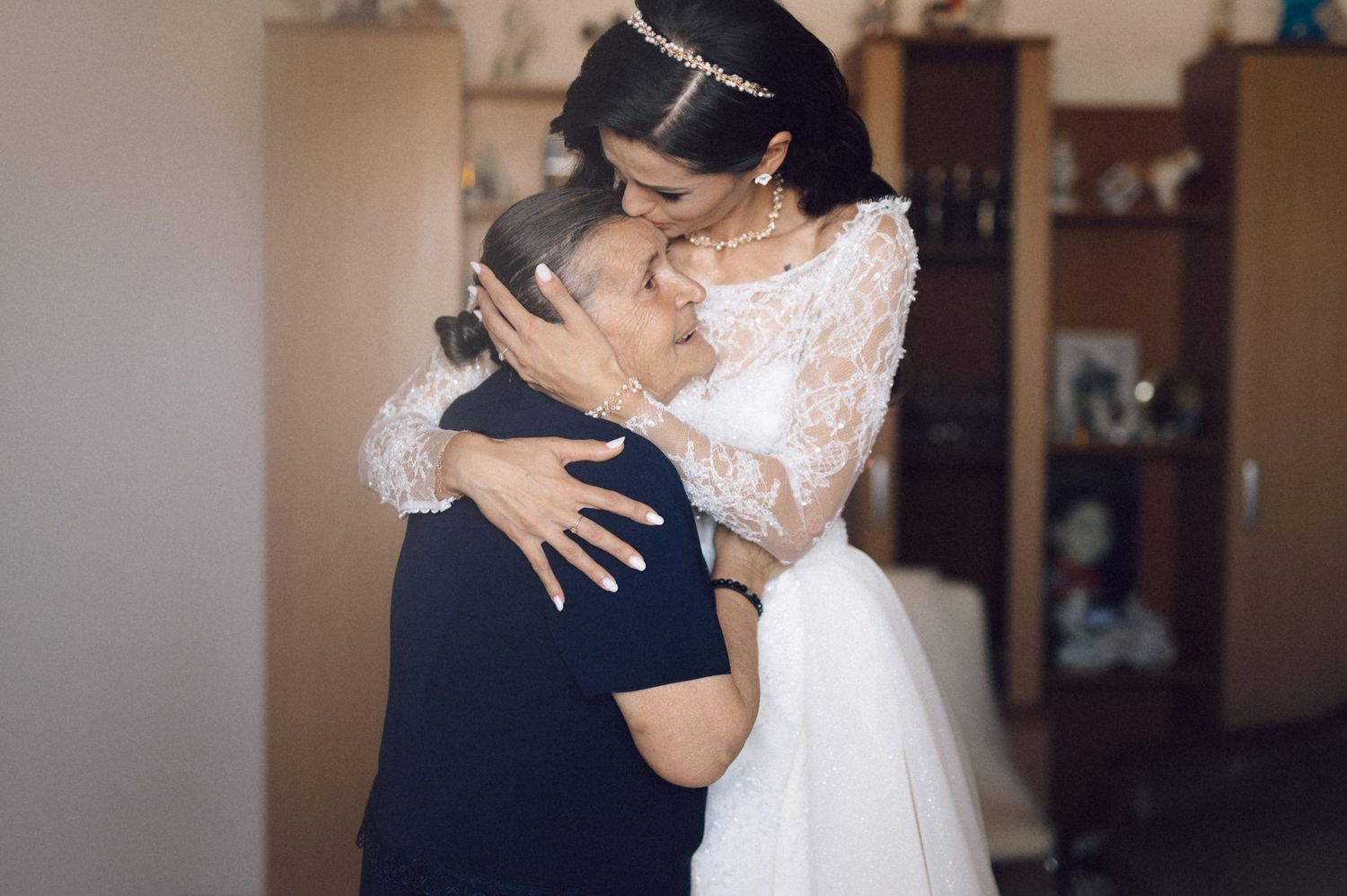 A tender embrace between two people, with one wearing an elegant white lace wedding dress and the other in dark attire.
