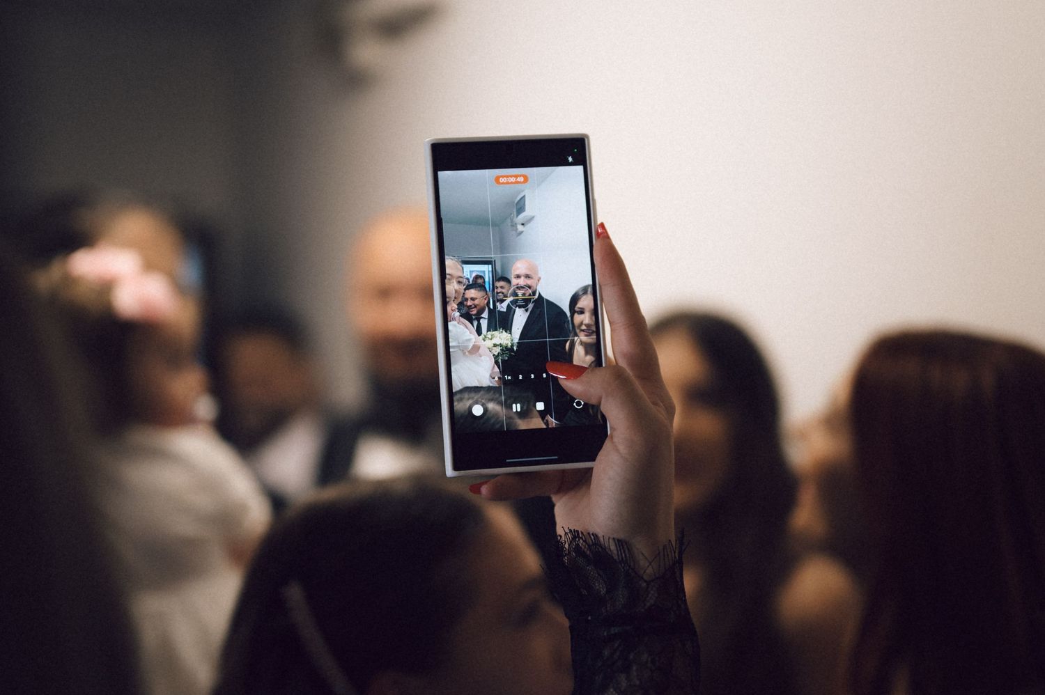 A person holds up a smartphone to record a performance or event in a dimly lit venue.