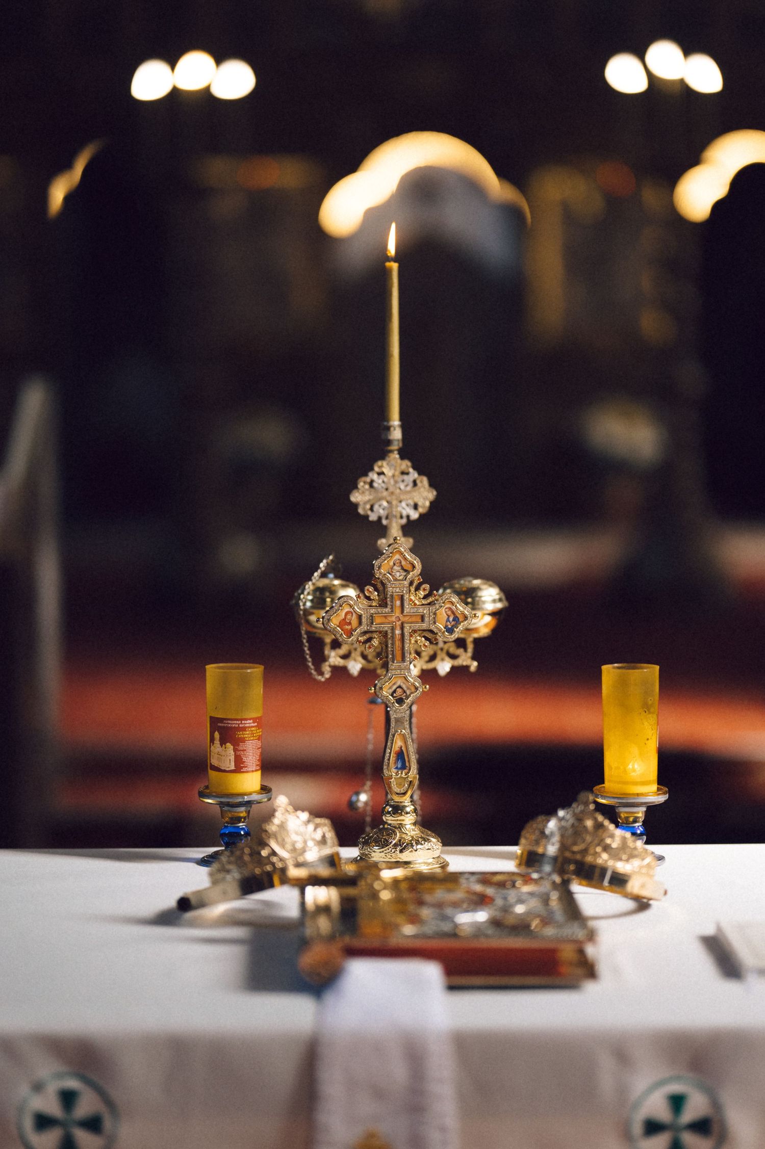 Ornate silver candlesticks with glowing candles arranged on a white tablecloth in a dimly lit restaurant setting.