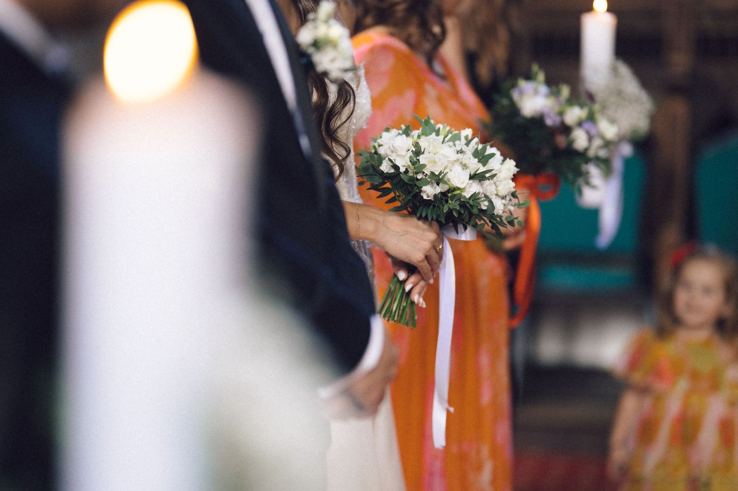 A person holding a bouquet of white flowers with greenery in front of an orange wall.