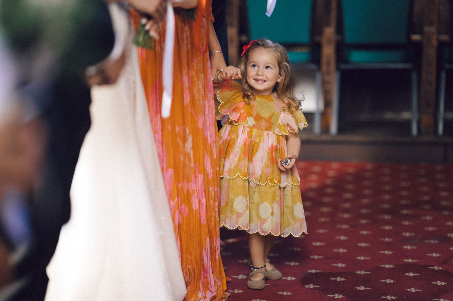 A young child wearing an orange and white dress walks down a red carpeted runway at a fashion show.