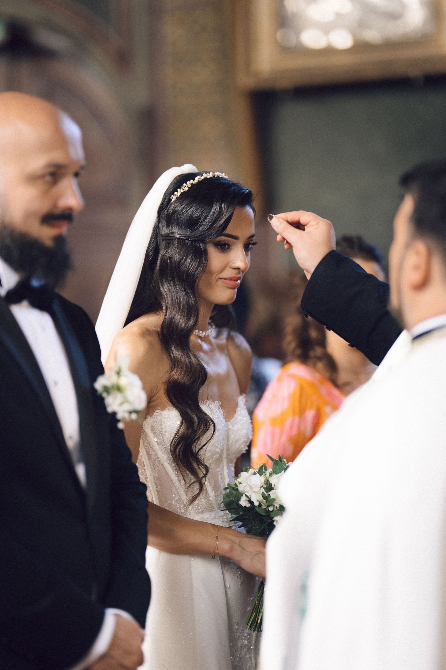 A bride in a white wedding dress with long wavy hair stands during a traditional church ceremony.