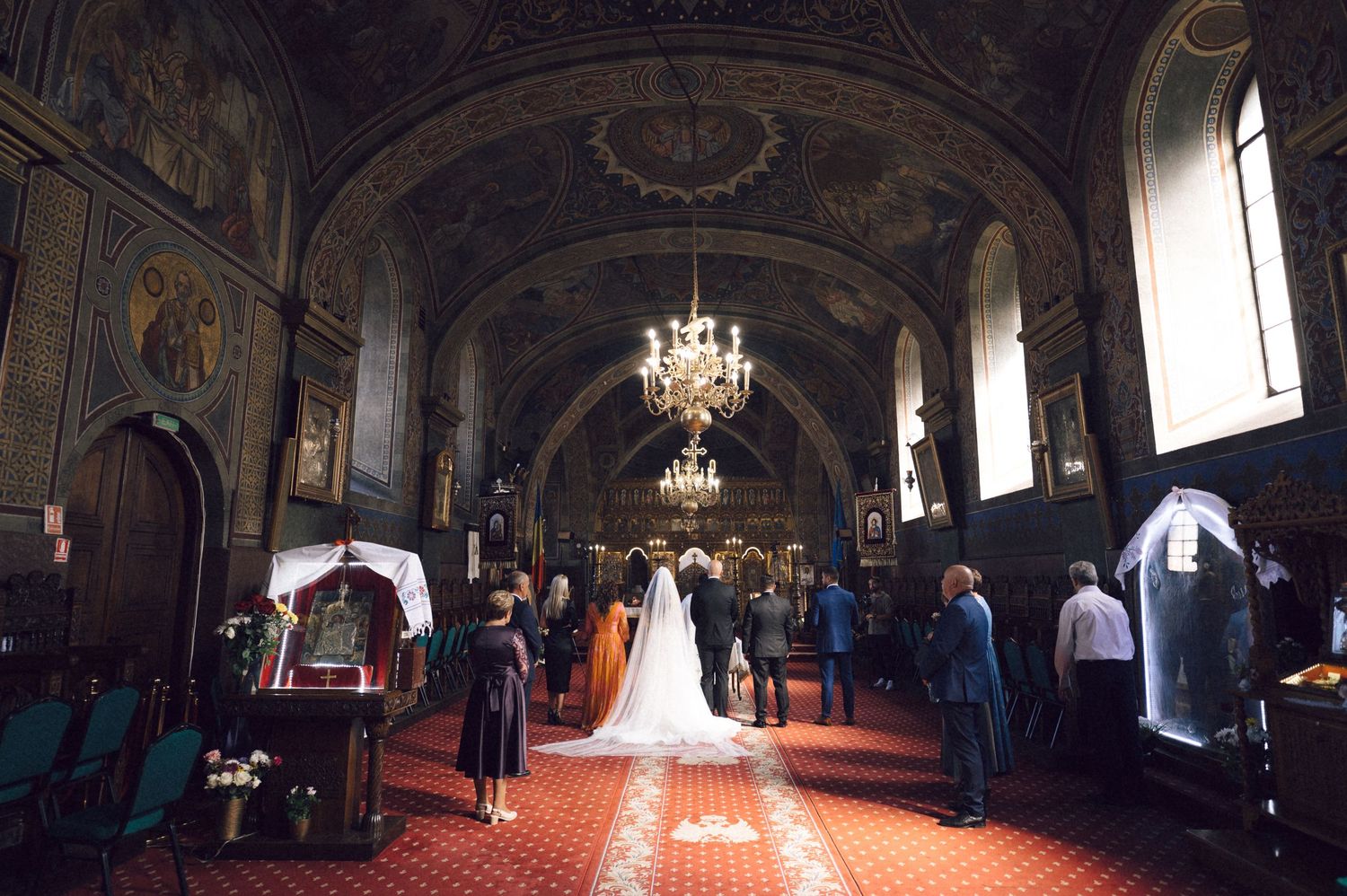 Panoramic view of an ornate church interior with high ceilings, chandeliers, and religious artwork during a ceremony.